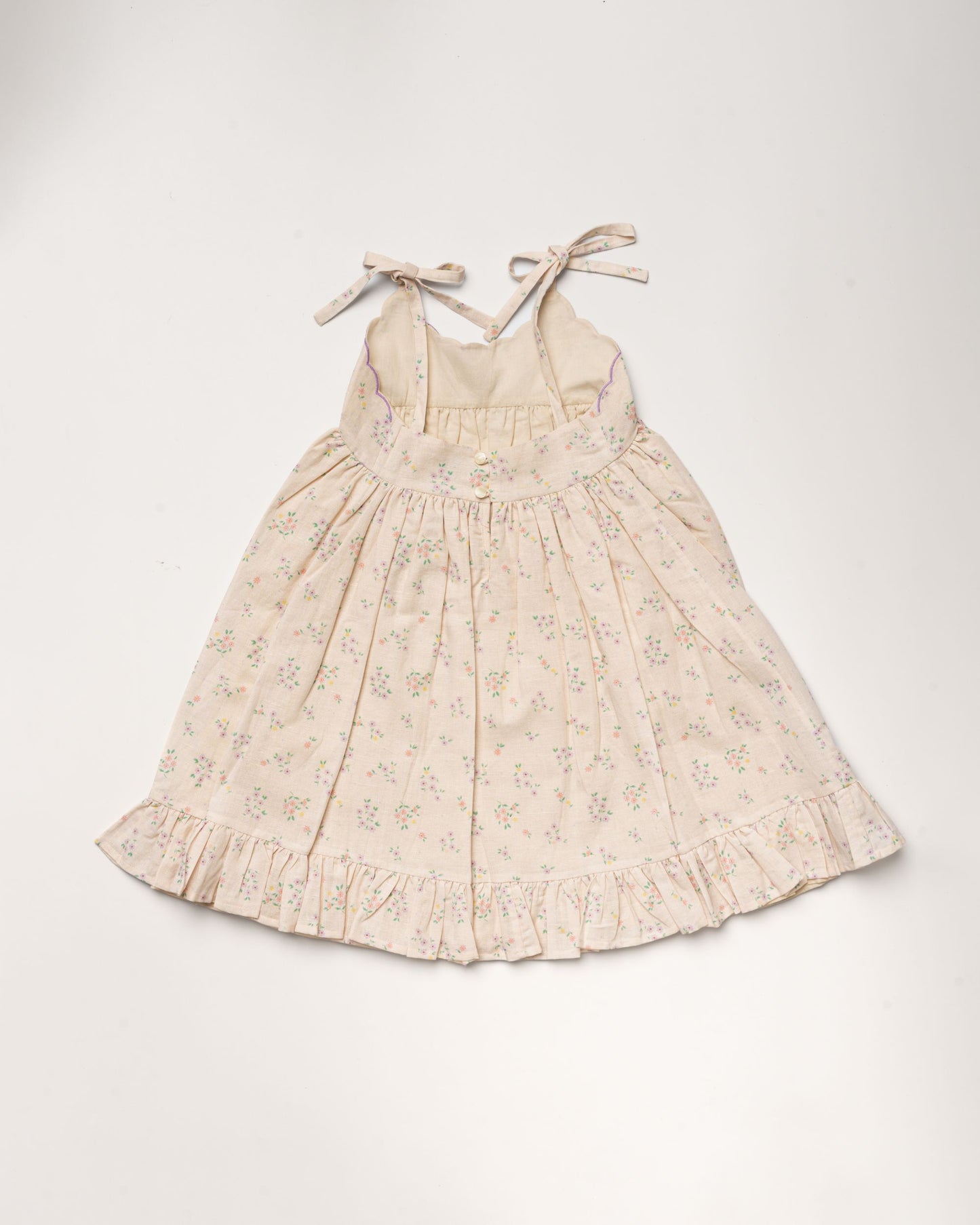 Early Sunday, Alena dress in Painted Bouquet color, made from printed 70% cotton 30% linen fabric, featuring tie-up shoulder straps, gathered flare, and ruffled hem, shown in a back flat-lay view.