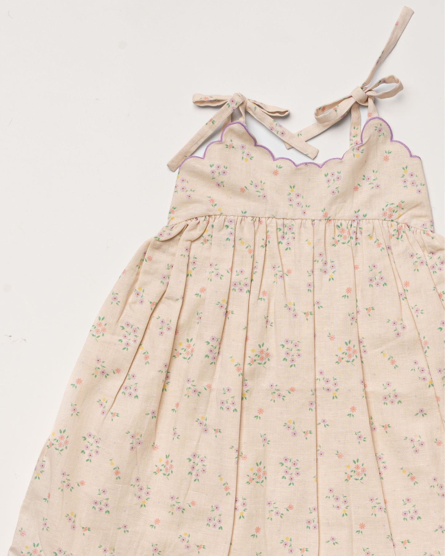 Early Sunday, Alena dress in Painted Bouquet color, made from printed 70% cotton 30% linen fabric, featuring tie-up shoulder straps, gathered flare, and ruffled hem, shown in a closeup flat-lay view.