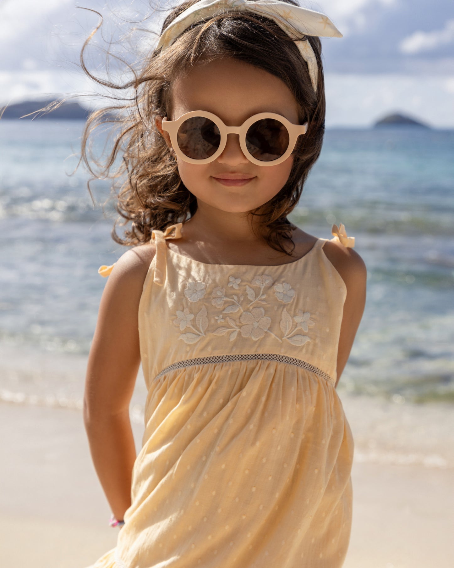 Early Sunday, Alice Dress in Vanilla color, made from Cotton Dobby Swiss Dots fabric, featuring sleeveless with adjustable tie-up straps and a tiered silhouette, shown in a close up shot of model wearing it