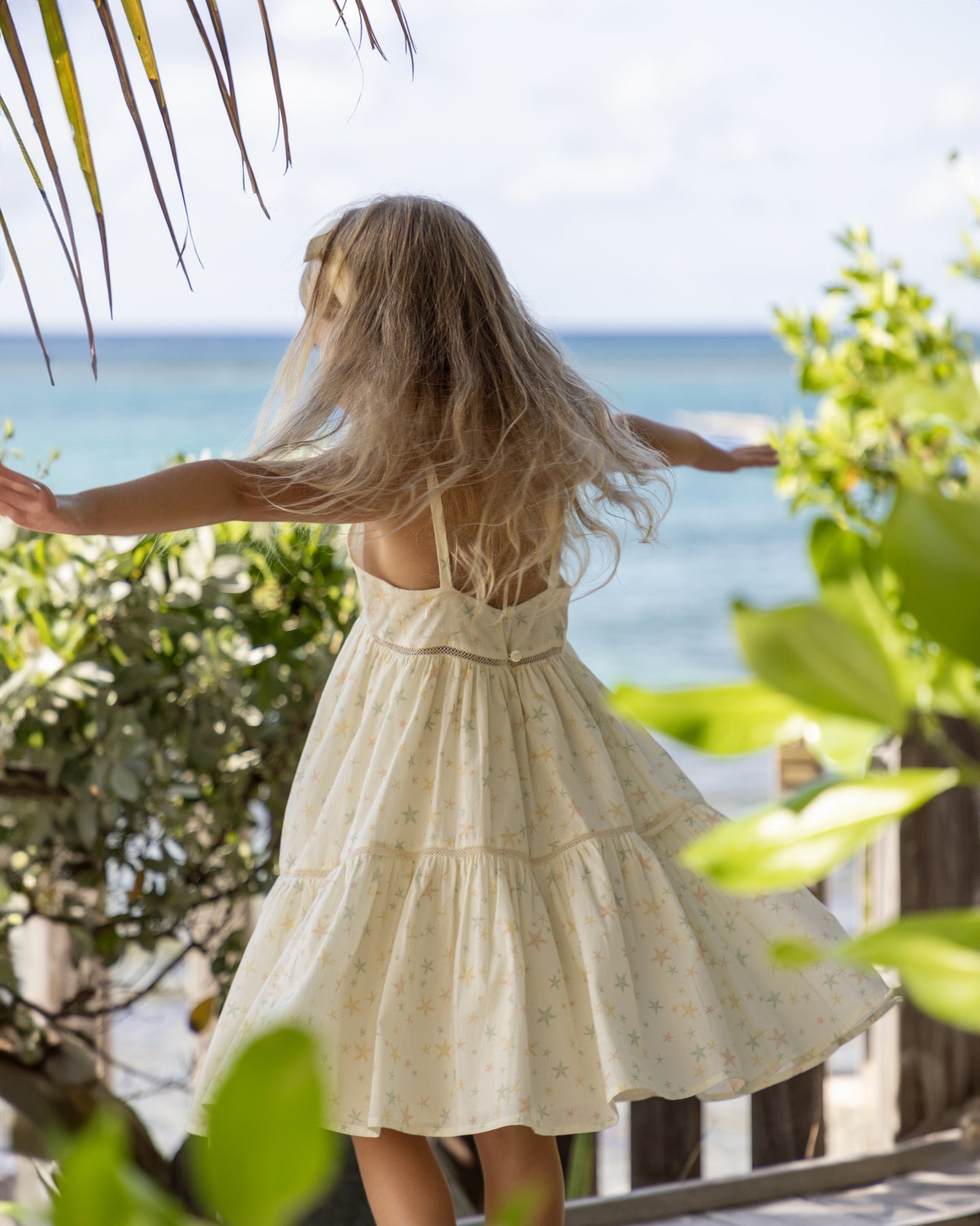 Early Sunday, Alice Dress in Star Fish print, made from Printed Cotton Cambric fabric, featuring sleeveless with adjustable tie-up straps and a tiered silhouette, shown in a back view of model wearing it