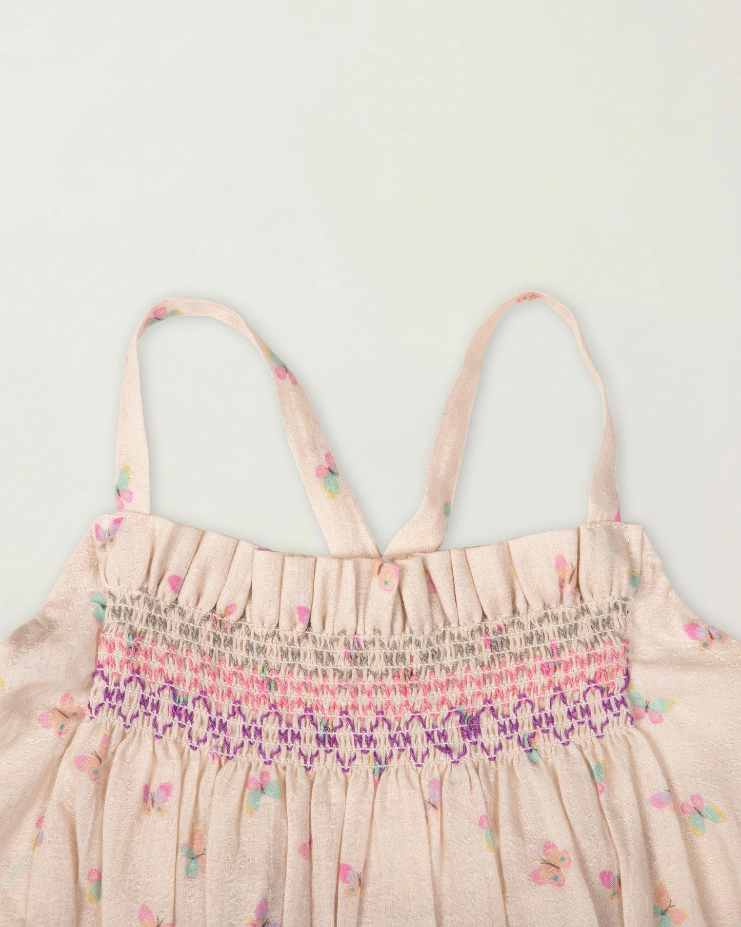 Early Sunday, Alisson Dress in butterfly print color, made from printed cotton tiny swiss dobby fabric, featuring smocked bodice, adjustable shoulder straps, sweet tassel accents, and a flowy gathered skirt, shown in a closeup flat-lay view.