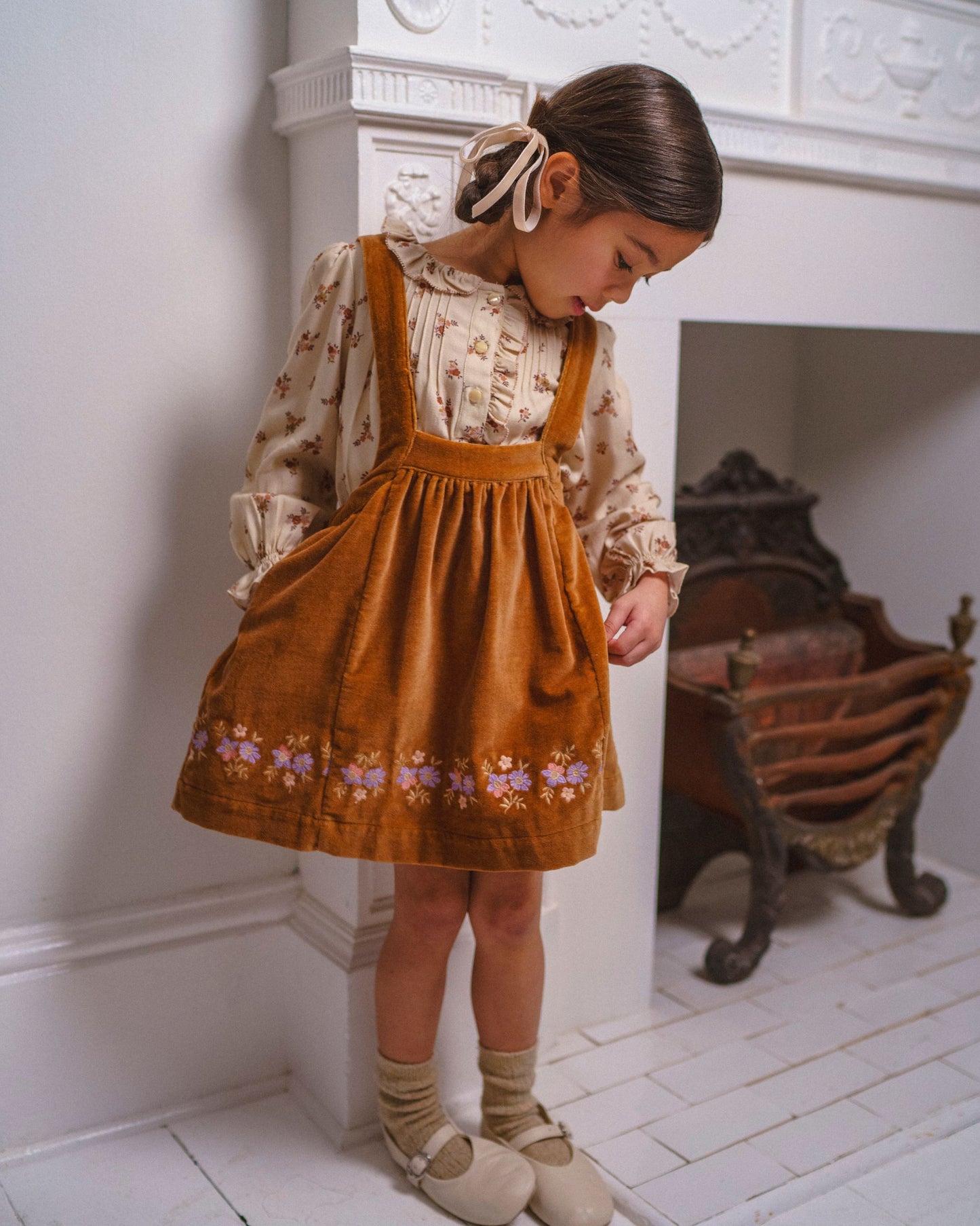 Early Sunday, Anni Skirt in Almond, made from Dyed Cotton Velvet fabric, featuring Delicate floral embroidery along the hem with playful cross-back straps, shown in a front view of a model wearing it in a studio setting