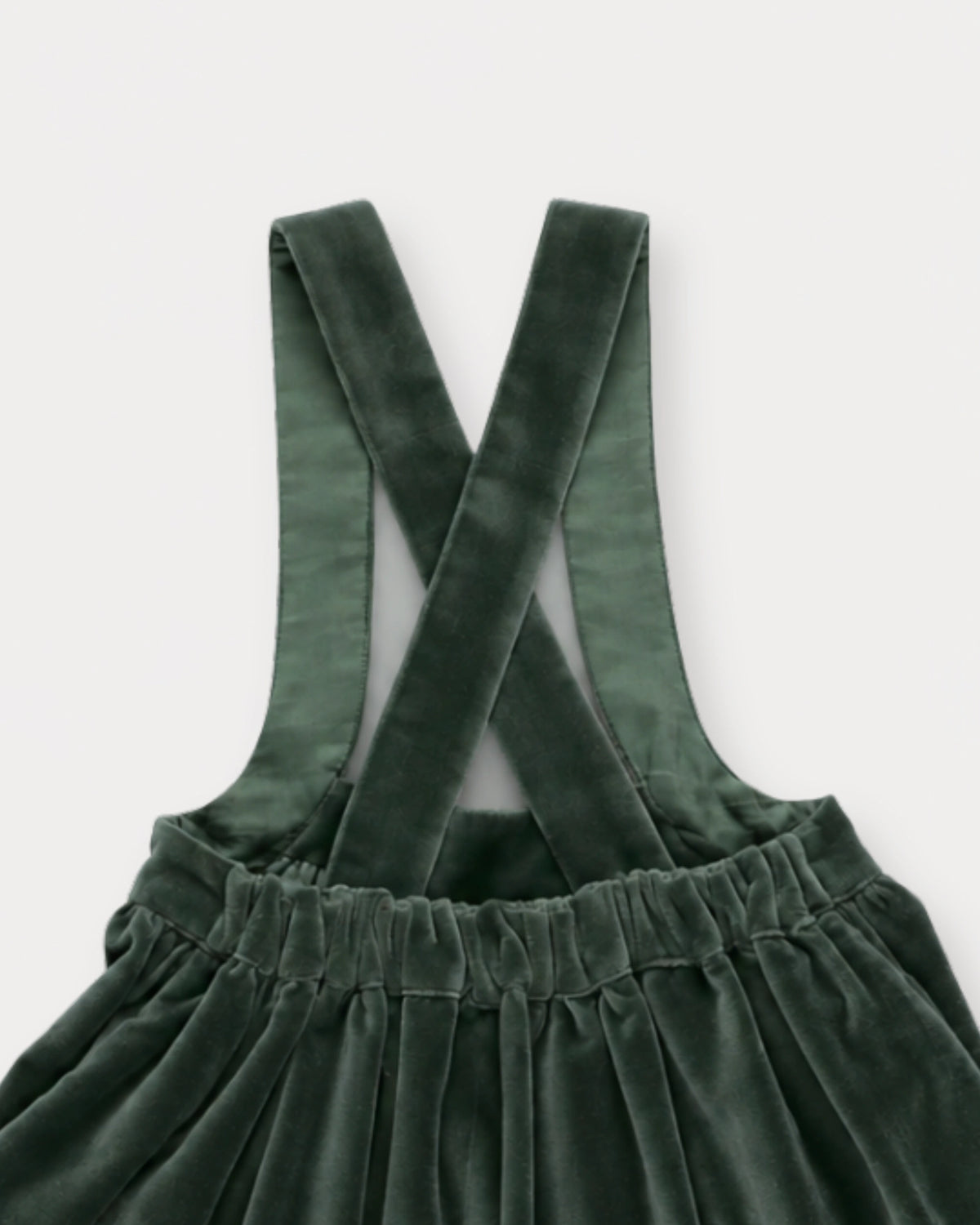 Early Sunday, Annie Skirt in Forest Green, made from Cotton Velvet Velour's fabric, featuring an A-line silhouette with adjustable cross-back straps and soft gathers, shown in a closeup flat-lay view