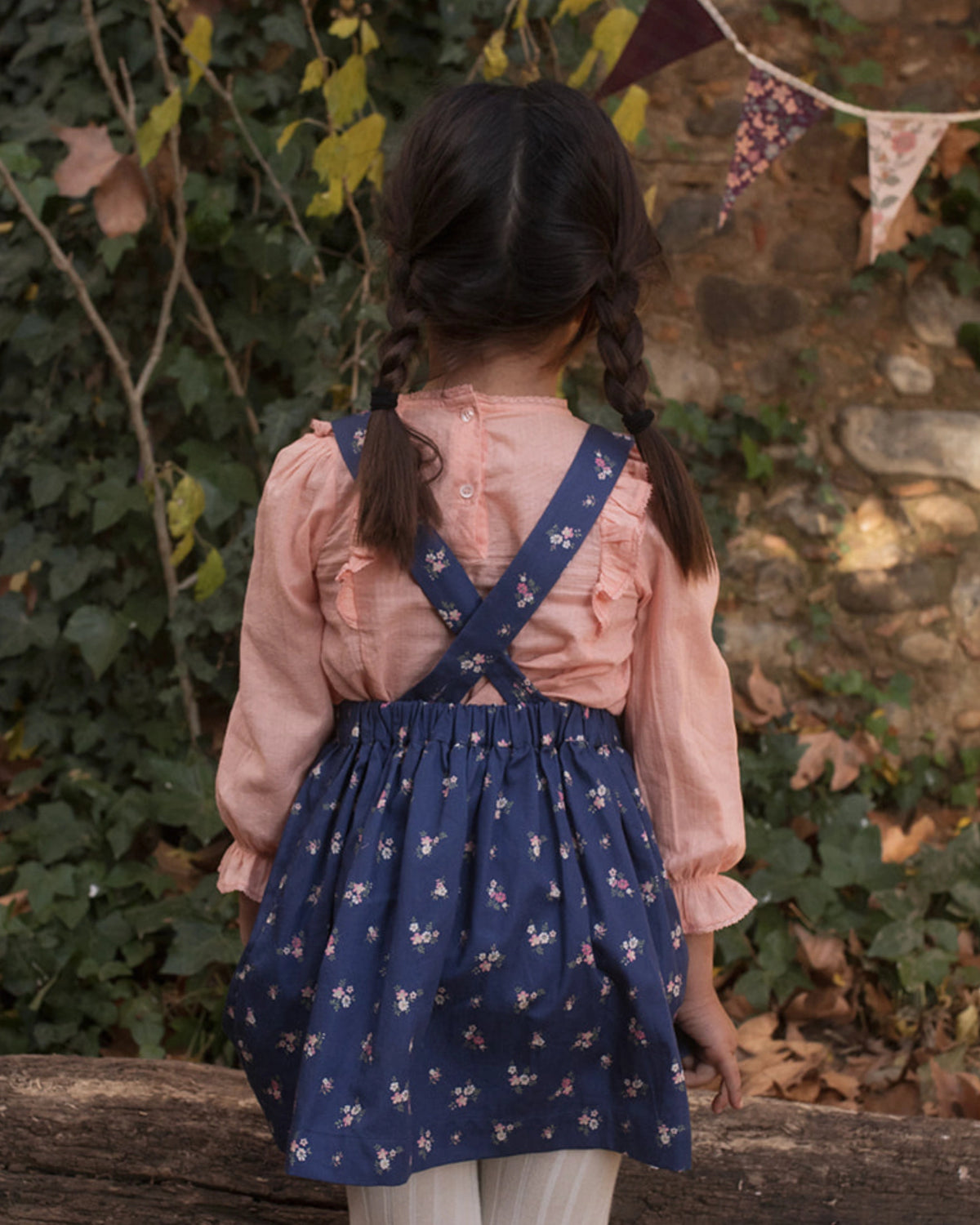 Early Sunday, Annie Skirt in Ditsy Bouquet Navy, made from Printed Cotton Satin fabric, featuring an A-line silhouette with adjustable cross-back straps and soft gathers, shown in a back view of model wearing it