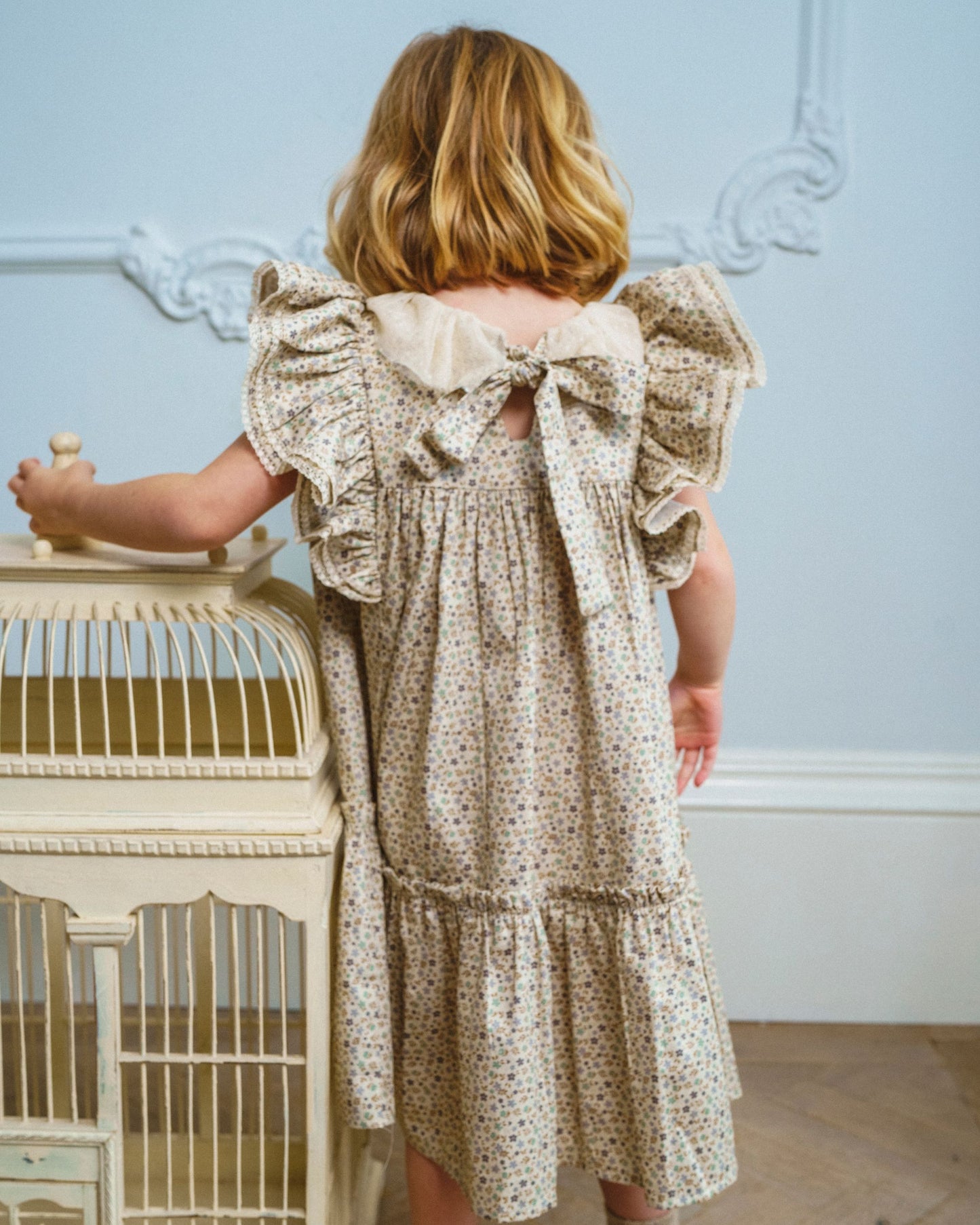 Early Sunday, Aurelia Dress in Miny Flowers print, made from Printed Cotton Satin fabric, featuring Layered ruffles with flutter sleeves, shown in a back view of model wearing