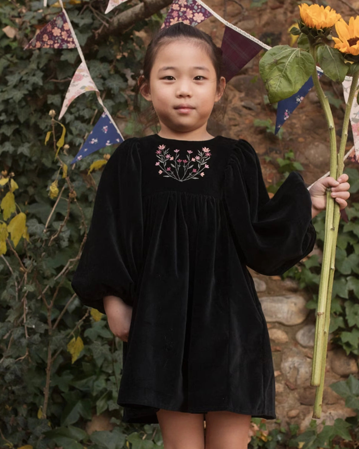 Early Sunday, Belle Dress in Black, made from Cotton Velvet Velour's fabric, featuring a flowing silhouette with puff sleeves and gentle gathers, shown in a front view of model wearing outdoors