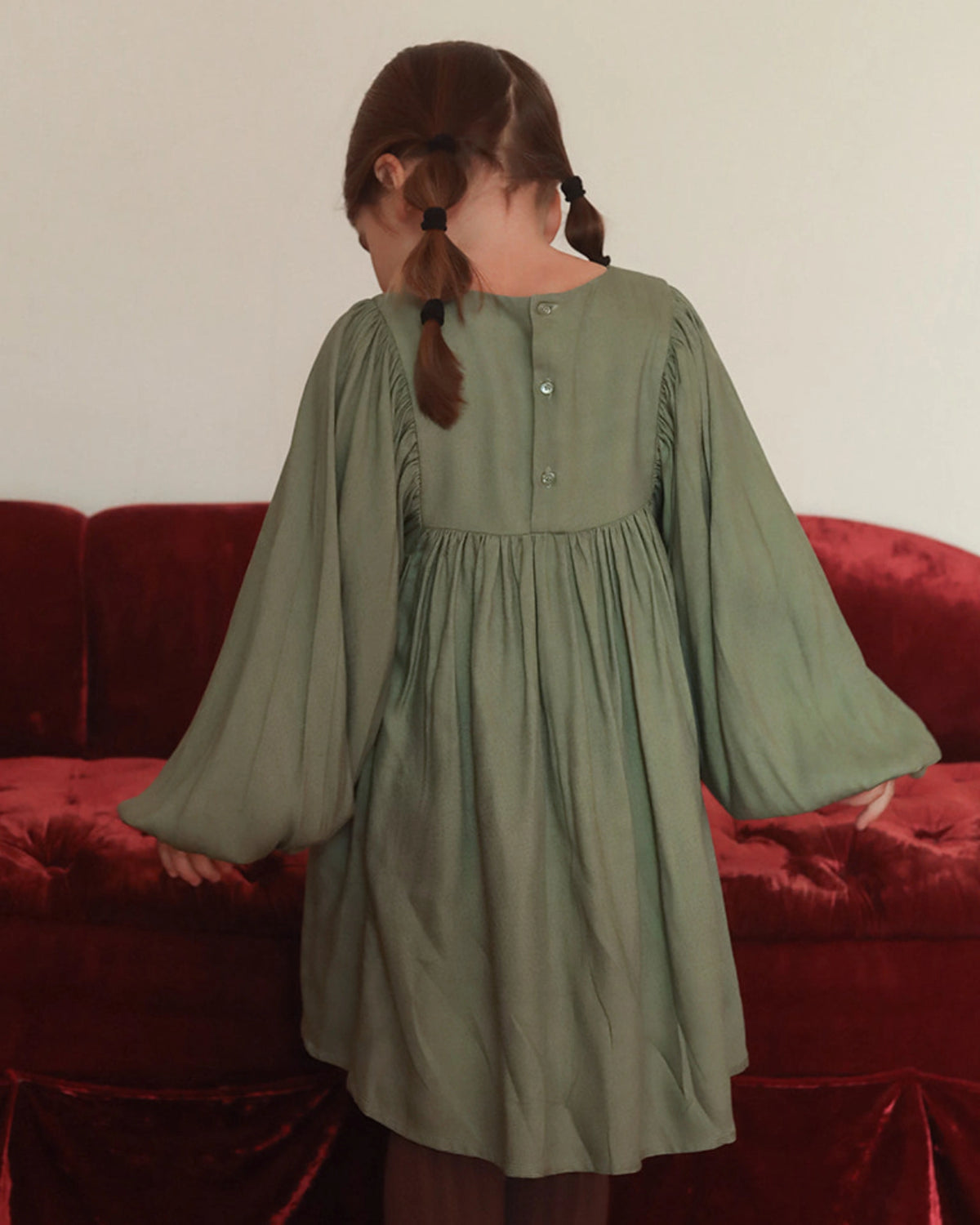 Early Sunday, Belle Dress in Sage Green, made from Viscose Twill fabric, featuring a square yoke bodice with puff sleeves and delicate gathered detailing, shown in a back view of model wearing it