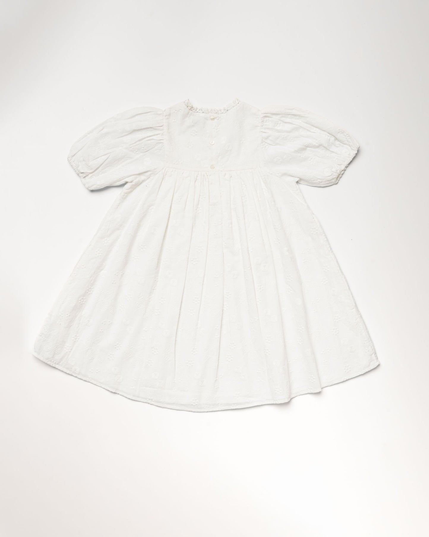 Early Sunday, Beth Dress in Ivory color, made from 100% cotton all over embroidered fabric, featuring Puff sleeves, contrast scalloped collar for a vintage touch, shown in a back flat-lay view.