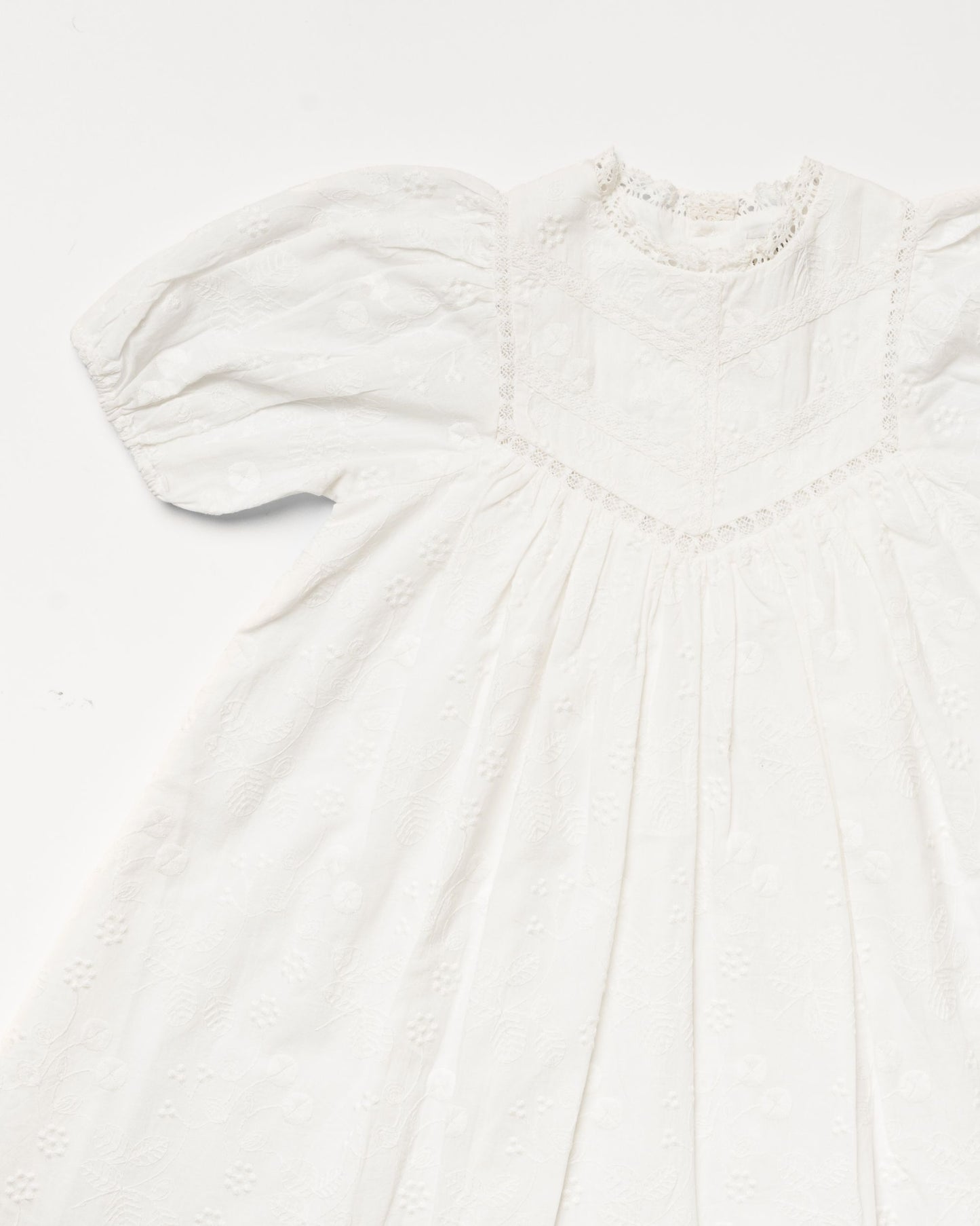 Early Sunday, Beth Dress in Ivory color, made from 100% cotton all over embroidered fabric, featuring Puff sleeves, contrast scalloped collar for a vintage touch, shown in a closeup flat-lay view.