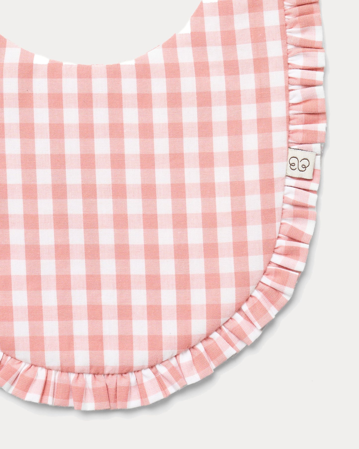 Early Sunday, Bib in Peony checks, made from Cotton Double Gauze fabric, shown in a closeup flat-lay view