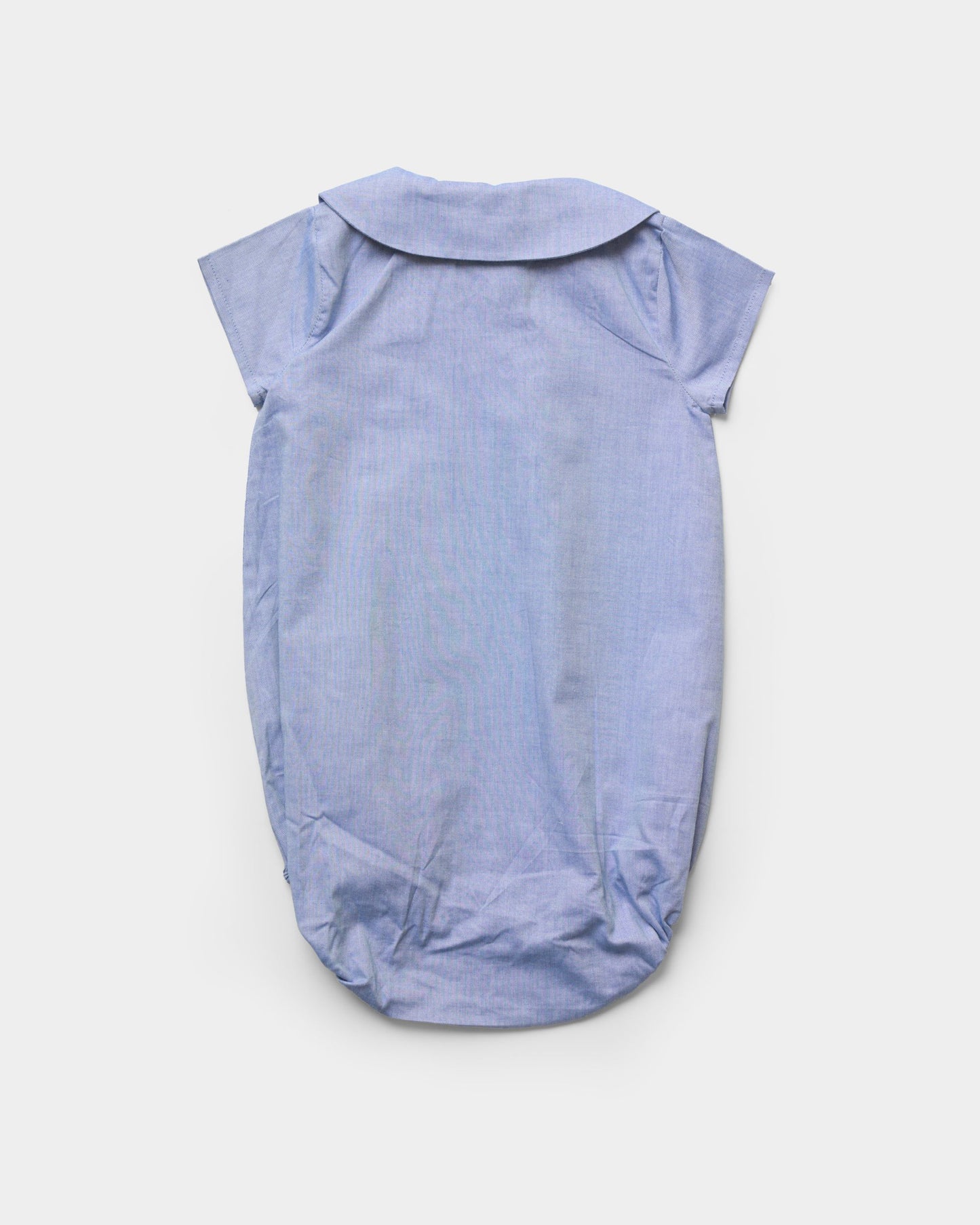 Early Sunday, Bobby Baby Romper in Summer Sky color, made from 100% Cotton Chambray fabric, featuring short sleeves with peter pan collar, shown in a back flat-lay view