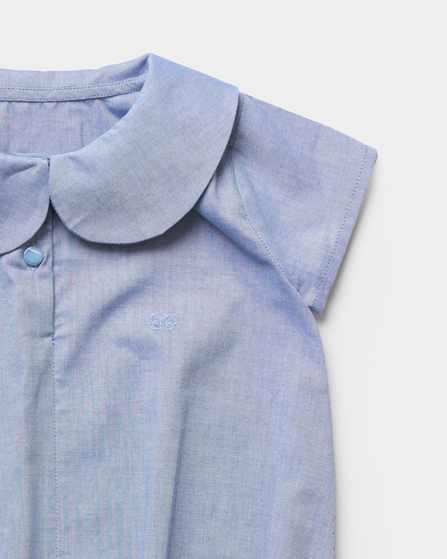 Early Sunday, Bobby Baby Romper in Summer Sky color, made from 100% Cotton Chambray fabric, featuring short sleeves with peter pan collar, shown in a closeup flat-lay view