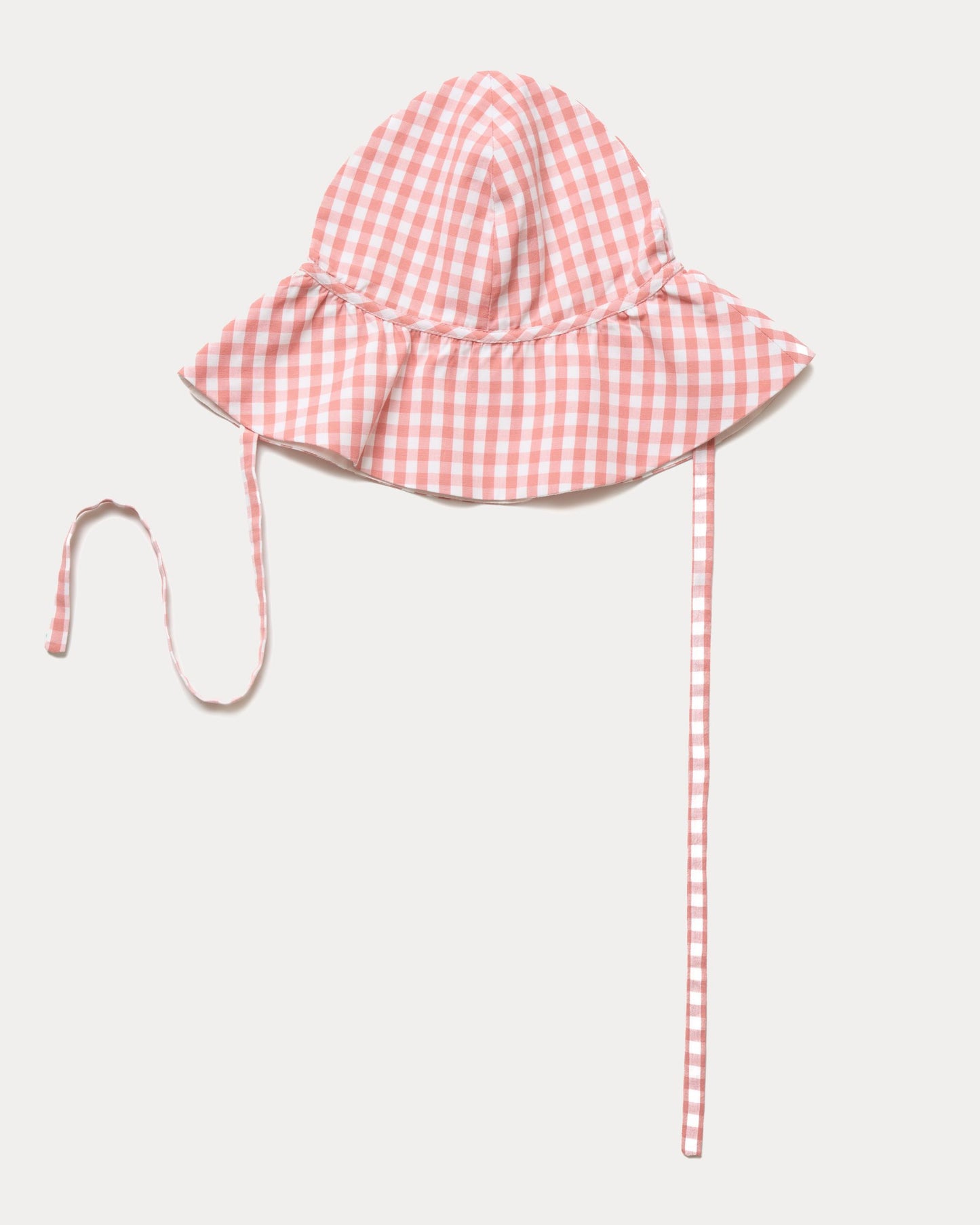 Early Sunday, Bonnie Hat Cap in Peony color, made from Gingham Check fabric, shown in an angled view with wide brim and tie straps