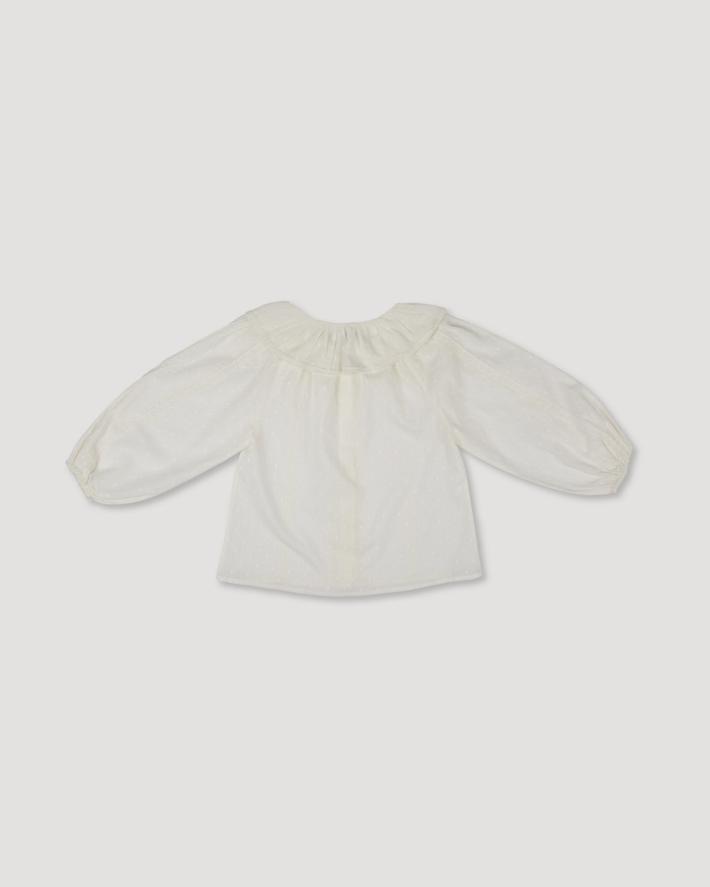 Early Sunday, Cecilia Blouse in Ecru color, made from Cotton Swiss Dobby fabric, featuring relaxed fit, frill neckline, long sleeves with elasticated cuffs, and MOP buttons, shown in a back flat-lay view