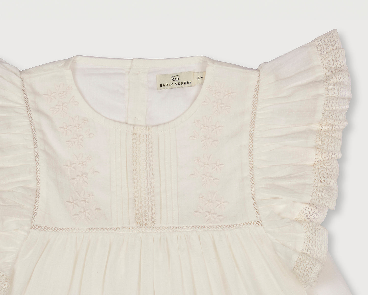 Early Sunday, Charlie Blouse in Ivory color, made from Cotton Tiny Swiss Dots fabric, featuring Flutter sleeves, pintuck detailing, and a flowy, gathered silhouette, shown in a closeup flat-lay view