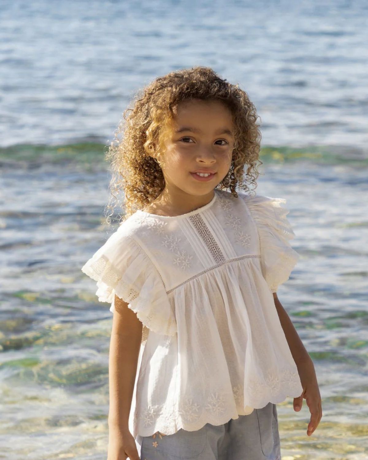 Early Sunday, Charlie Blouse in Ivory color, made from Cotton Tiny Swiss Dots fabric, featuring flutter sleeves, pintuck detailing, and a flowy, gathered silhouette, shown in a front view of model wearing it