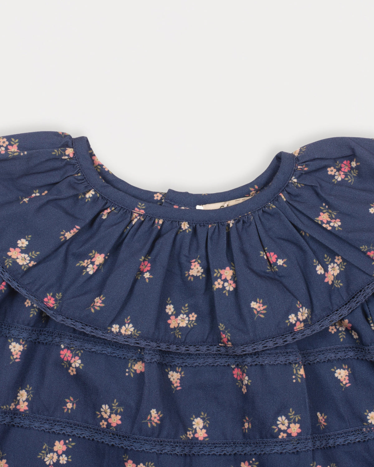 Early Sunday, Daisy Baby Blouse & Bloomer Set in Ditsy Bouquet Navy, made from Printed Cotton Satin fabric, featuring a frilly neckline with detailed lace yoke & gathered sleeves, shown in a closeup flat-lay view