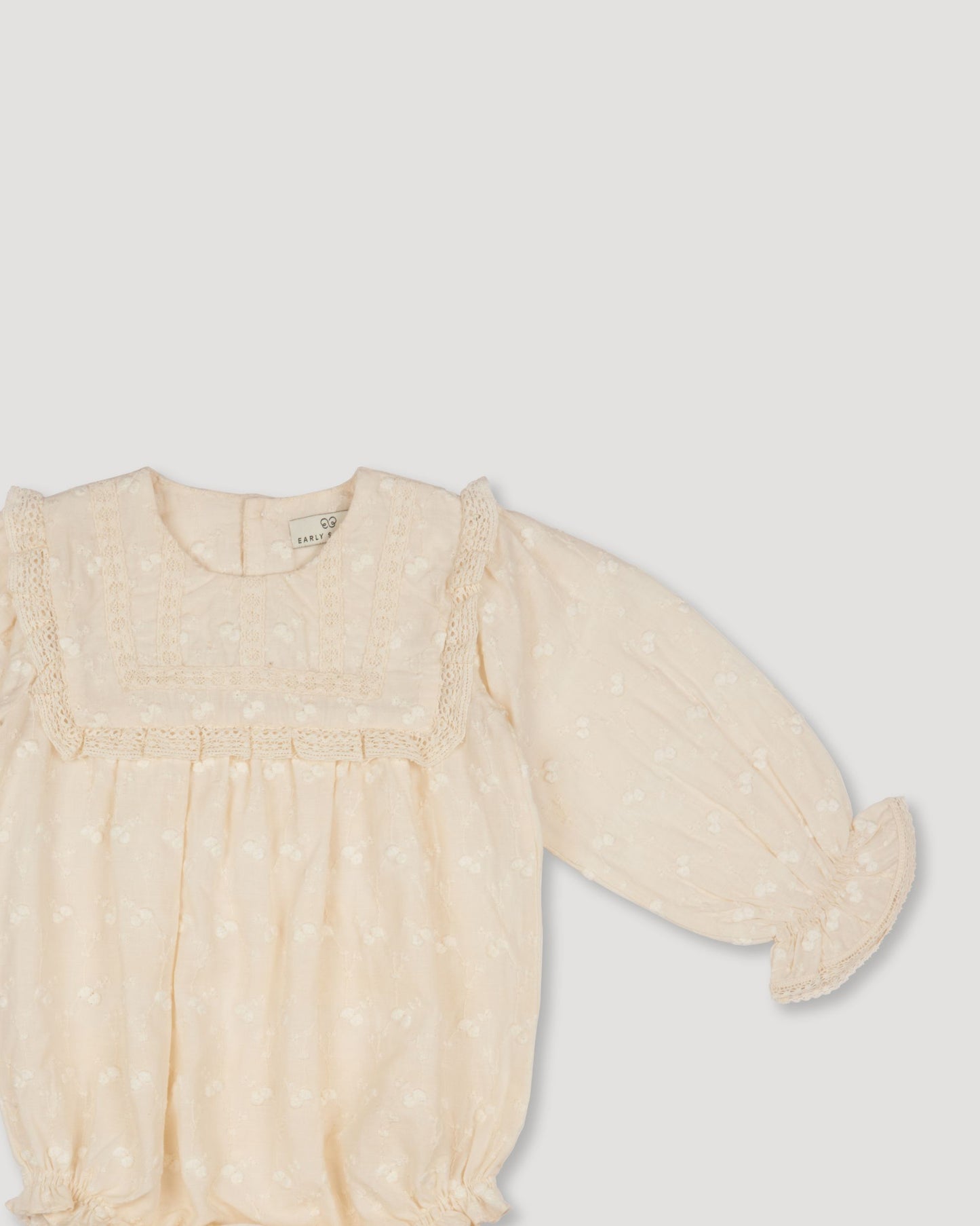 Early Sunday, Dolly Baby Bubble Romper in Hazelnut Cream color, made from All-over Embroidered Cotton Cambric fabric, featuring smocked sleeves & a square lace yoke, shown in a closeup flat-lay view
