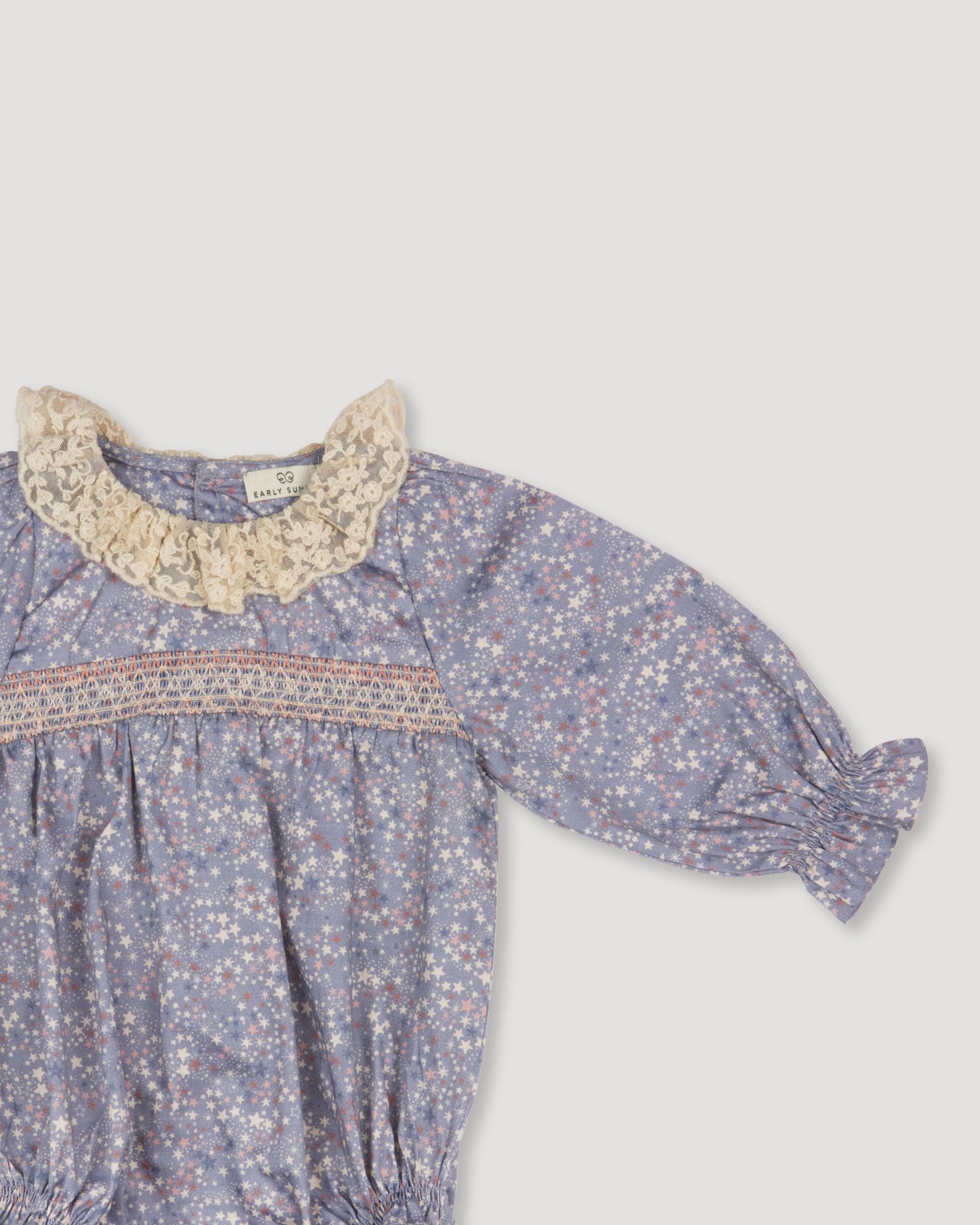 Early Sunday, Ellie Baby Bubble Romper in Celestial print, made from Printed 60s cotton satin fabric, featuring smocked sleeves with laced neckline, shown in a closeup flat-lay view