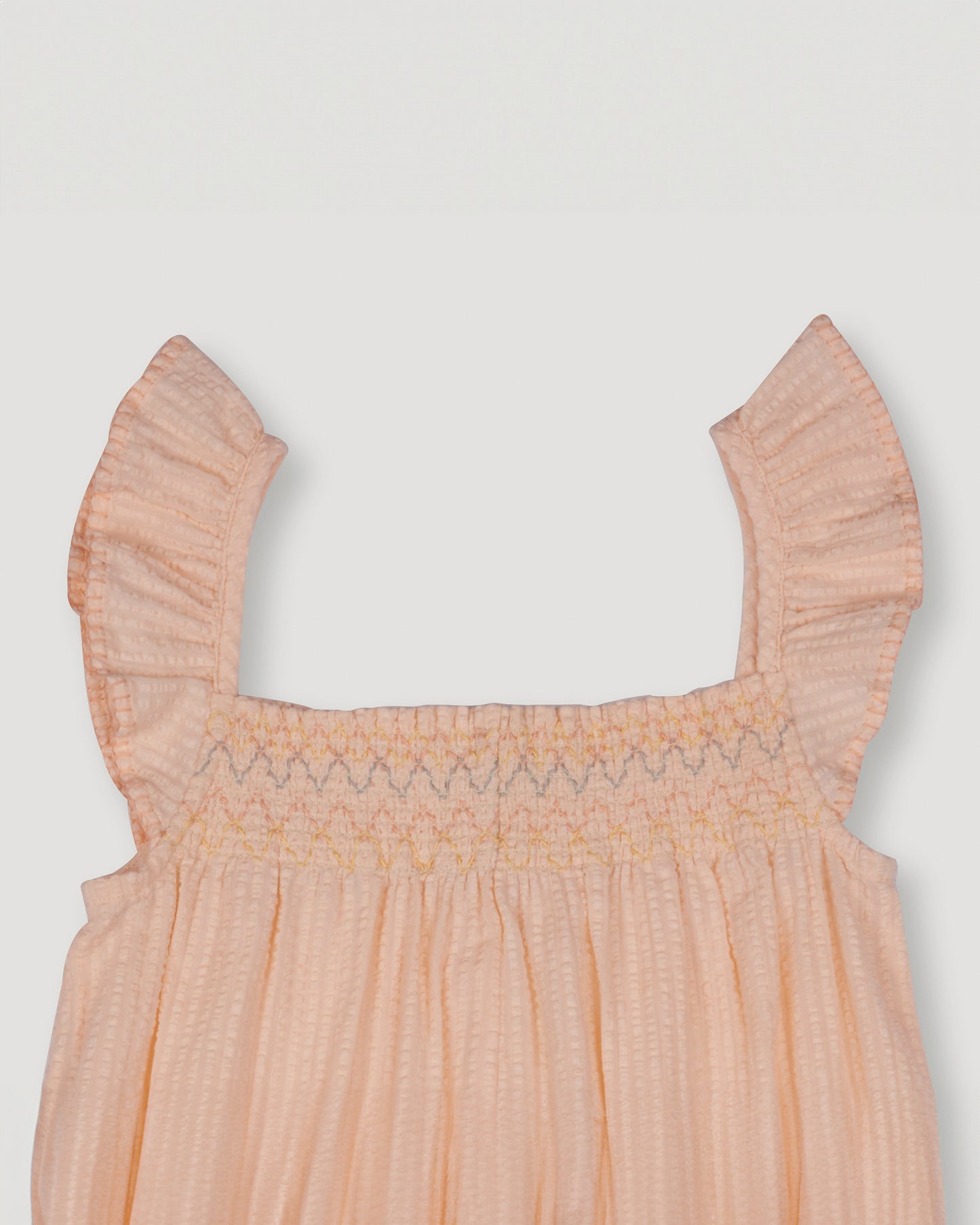 Early Sunday, Emma Baby Smocked Overalls Romper in Warm Sand color, made from Cotton Seersucker fabric, featuring a relaxed fit with smocked chest band & frilled sleeves, shown in a closeup flat-lay view