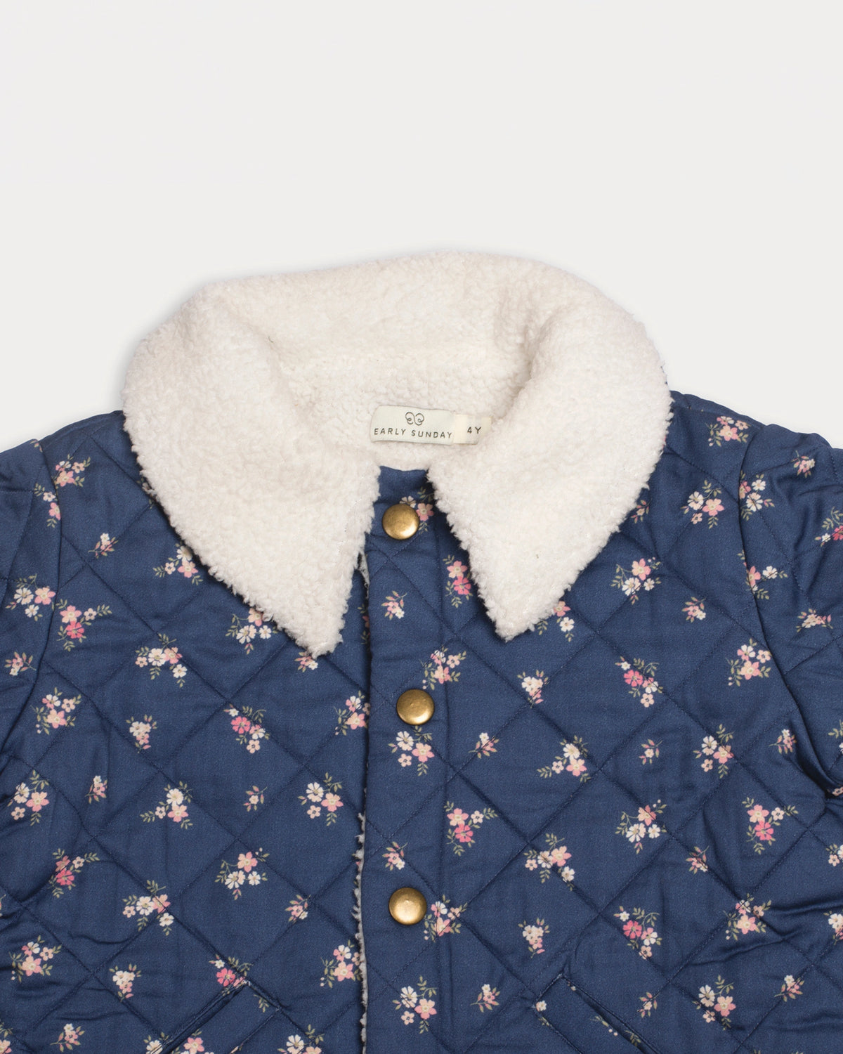 Early Sunday, Esmée Jacket in Ditsy Bouquet Navy, made from Printed Cotton Satin fabric, featuring a quilted layer with floral detailing, shown in a closeup flat-lay view
