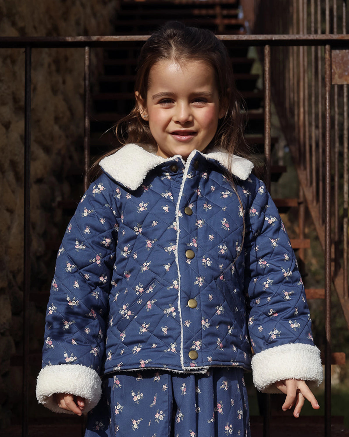 Early Sunday, Esmée Jacket in Ditsy Bouquet Navy, made from Printed Cotton Satin fabric, featuring a quilted layer with floral detailing, shown in a front view of model wearing outdoors