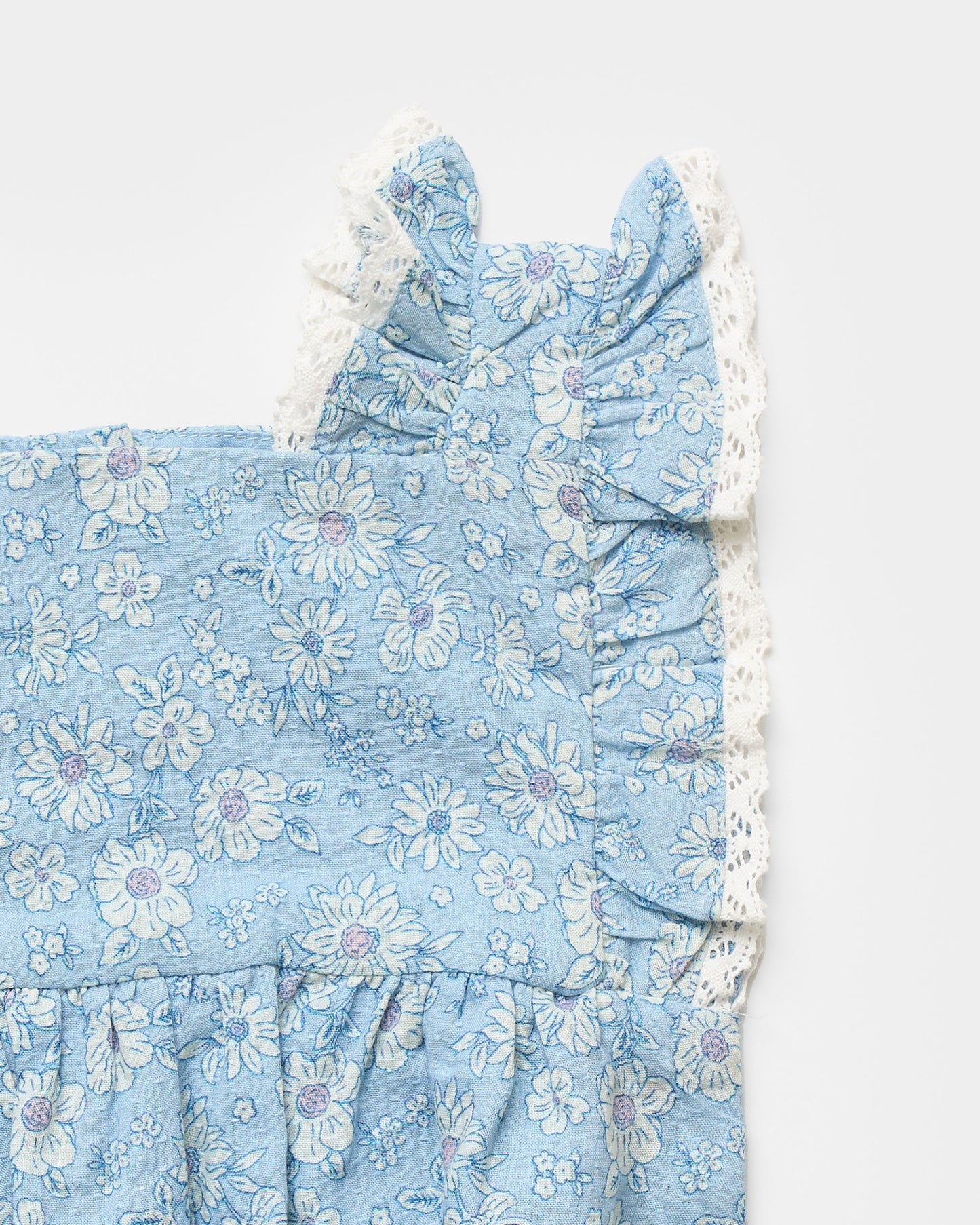 Early Sunday, Eva Baby Romper in Tonal Floral Blue color, made from 100% Cotton Swiss Dobby Tiny Dots fabric, featuring a sleeveless design with lace border, shown in a closeup flat-lay view