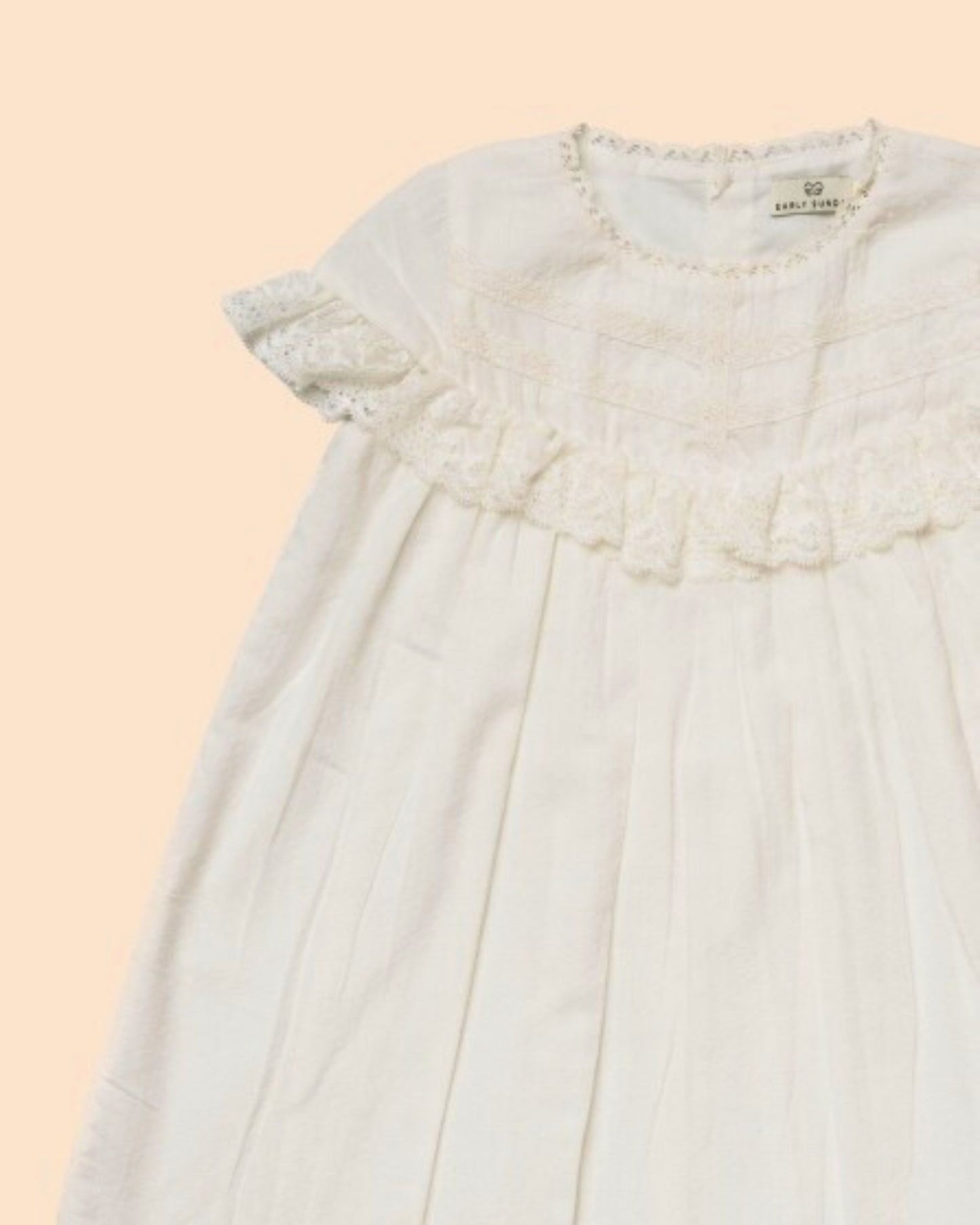 Early Sunday, Faustine Dress in Ivory color, made from 100% cotton swiss dobby tiny dots fabric, featuring Soft gathers with delicate ruffle accents, shown in a closeup flat-lay view