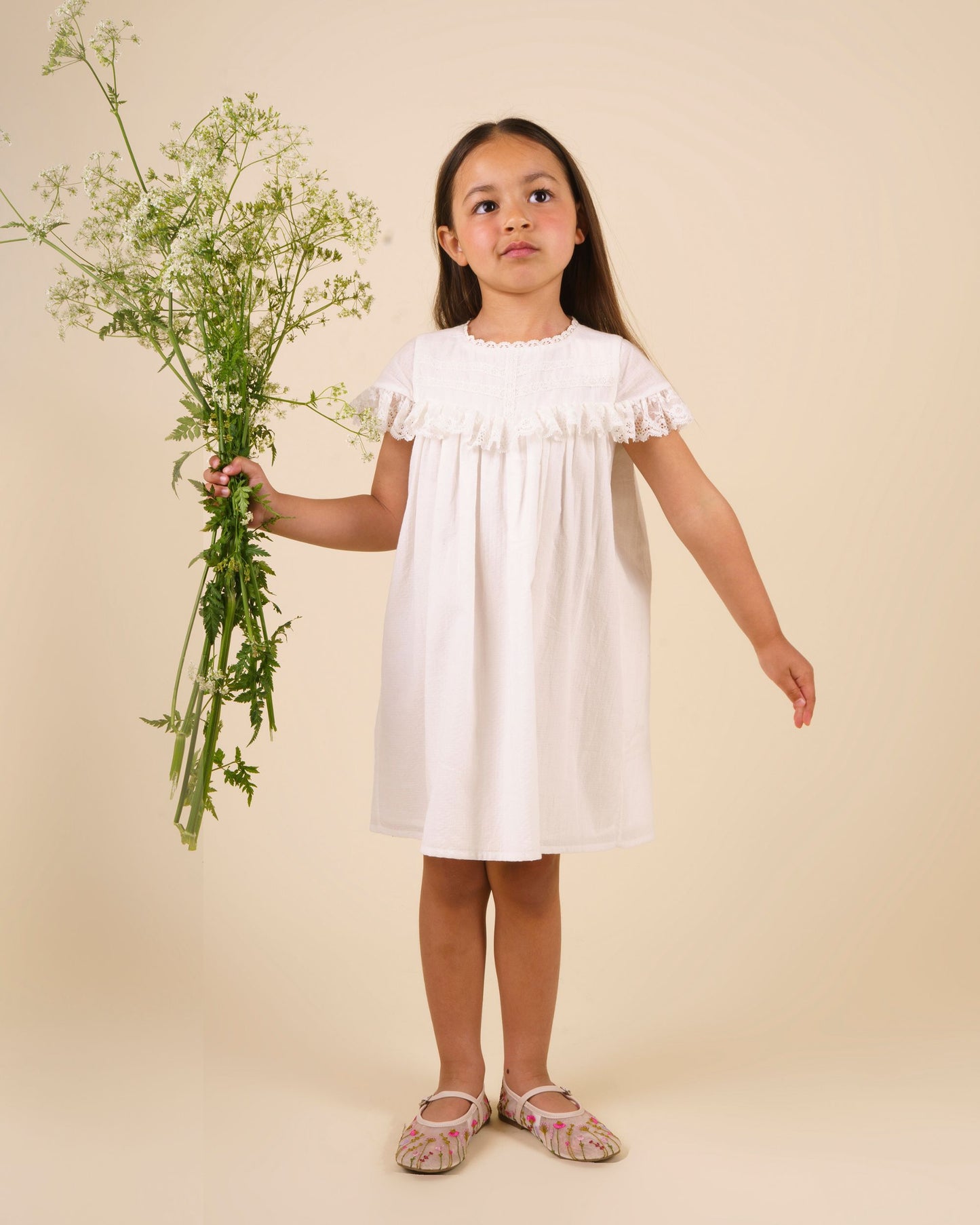 Early Sunday, Faustine Dress in Ivory color, made from 100% cotton swiss dobby tiny dots fabric, featuring Soft gathers with delicate ruffle accents, shown in a front view of model wearing it