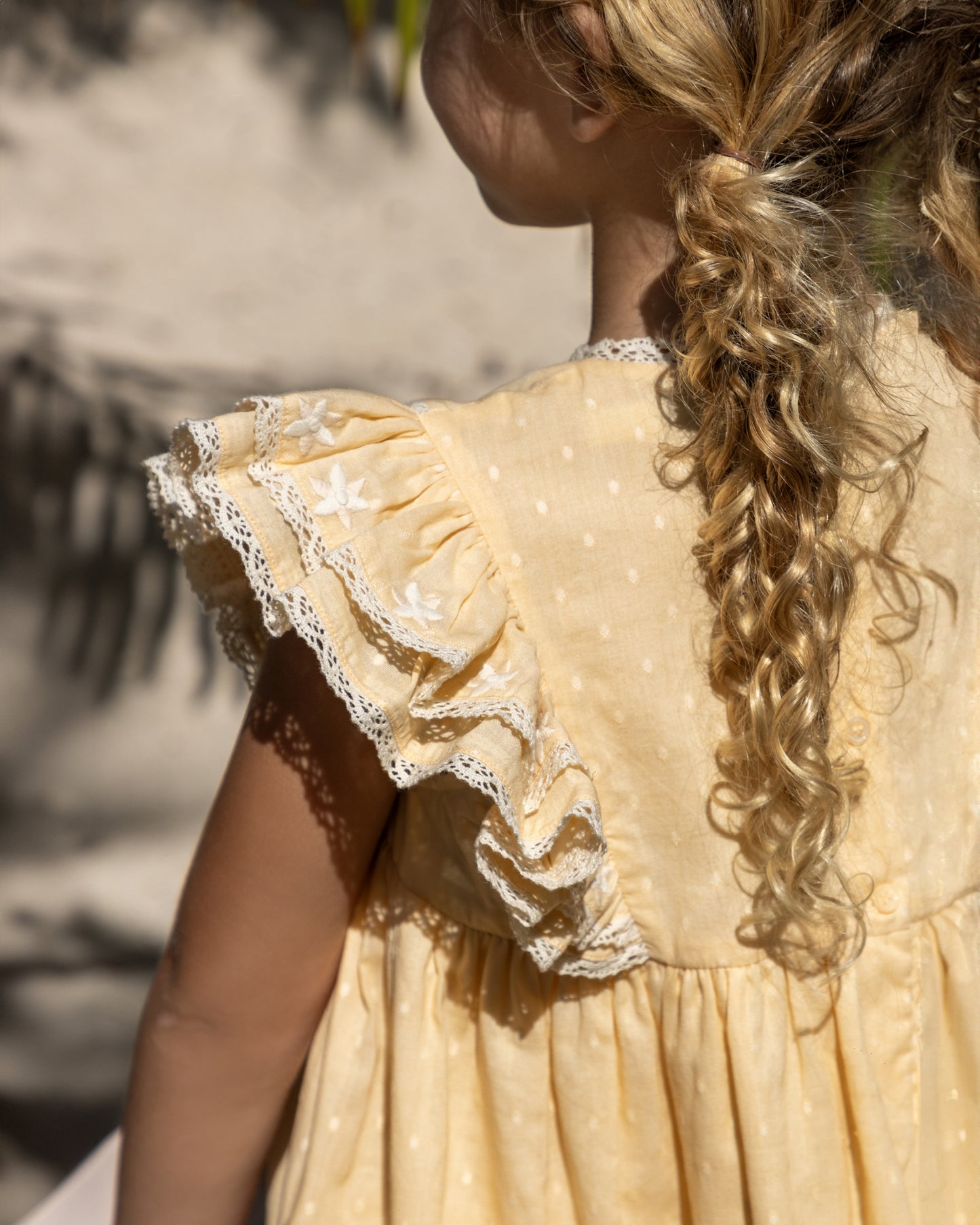 Early Sunday, Georgia Dress in Vanilla color, made from Cotton Dobby Swiss Dots fabric, featuring Flutter sleeves, pintuck detailing, and a flowy, gathered silhouette, shown in a back view of model wearing it
