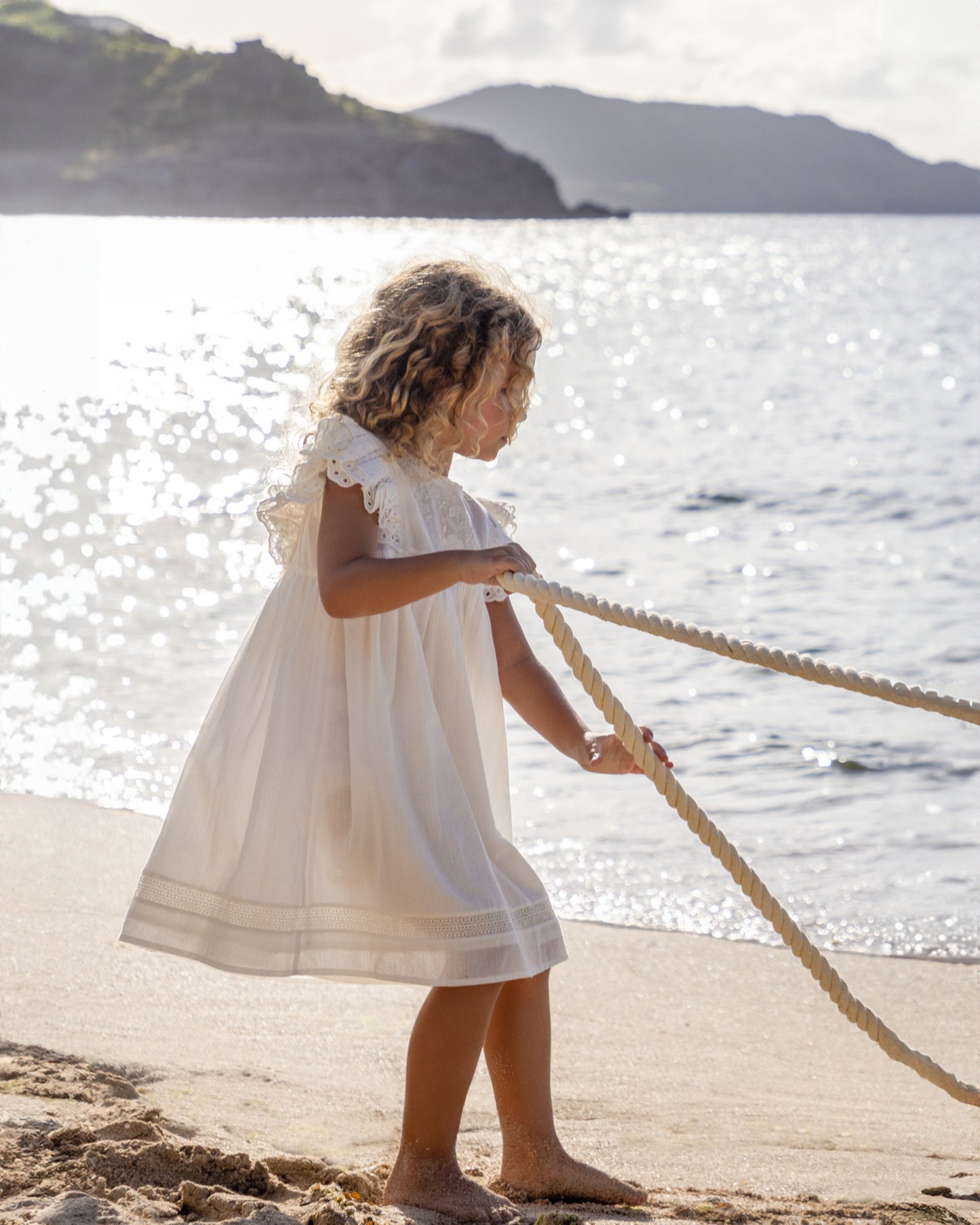 Early Sunday, Georgia Dress in Ivory color, made from Cotton Tiny Swiss Dots fabric, featuring Flutter sleeves, embroidered floral accents, lace hem detailing, and a flowy silhouette., shown in a outdoor shot of model wearing