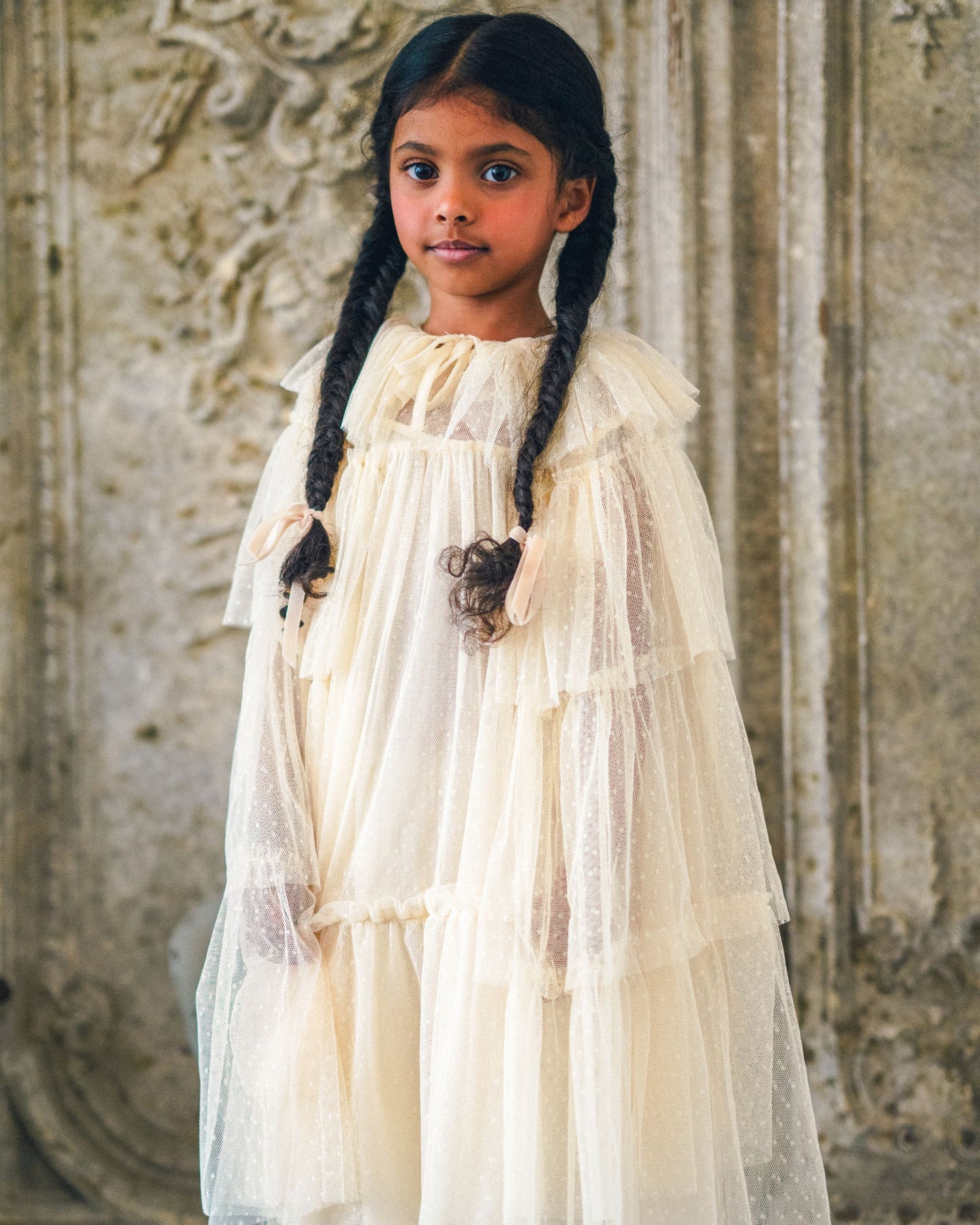 Early Sunday, Grace Cape in Hazelnut Cream, made from Dyed Nylon Mesh Dobby fabric, featuring Tiered ruffles create volume and whimsical movement, shown in a front view of a model wearing it in a studio setting
