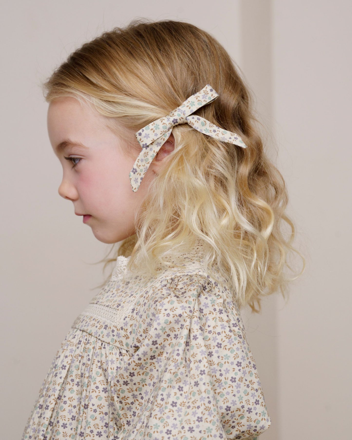 Early Sunday, Grace Clip in Mini Flowers print, made from Printed 60s Cotton Satin fabric, featuring a set of two bow clips with a secure fit, shown in a side view of a model wearing it in a studio setting