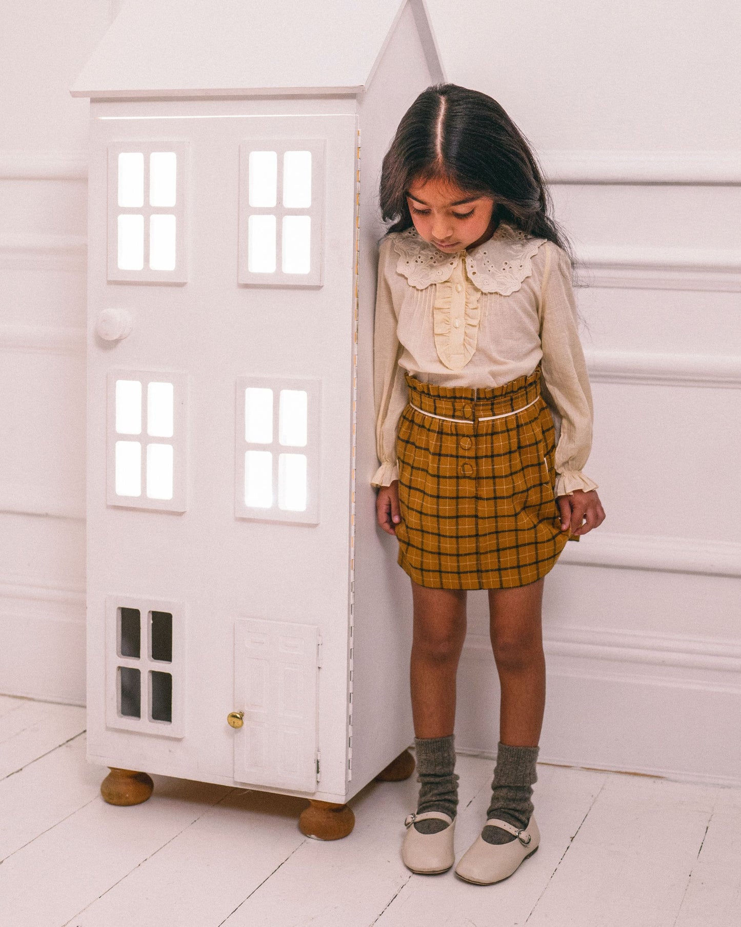 Early Sunday, Hilda Skirt in Almond Checks, made from Cotton Yarn Dyed Brushed Checks fabric, featuring A-line shape with a gathered elastic waistband for comfort, shown in a front view of a model wearing it in a studio setting