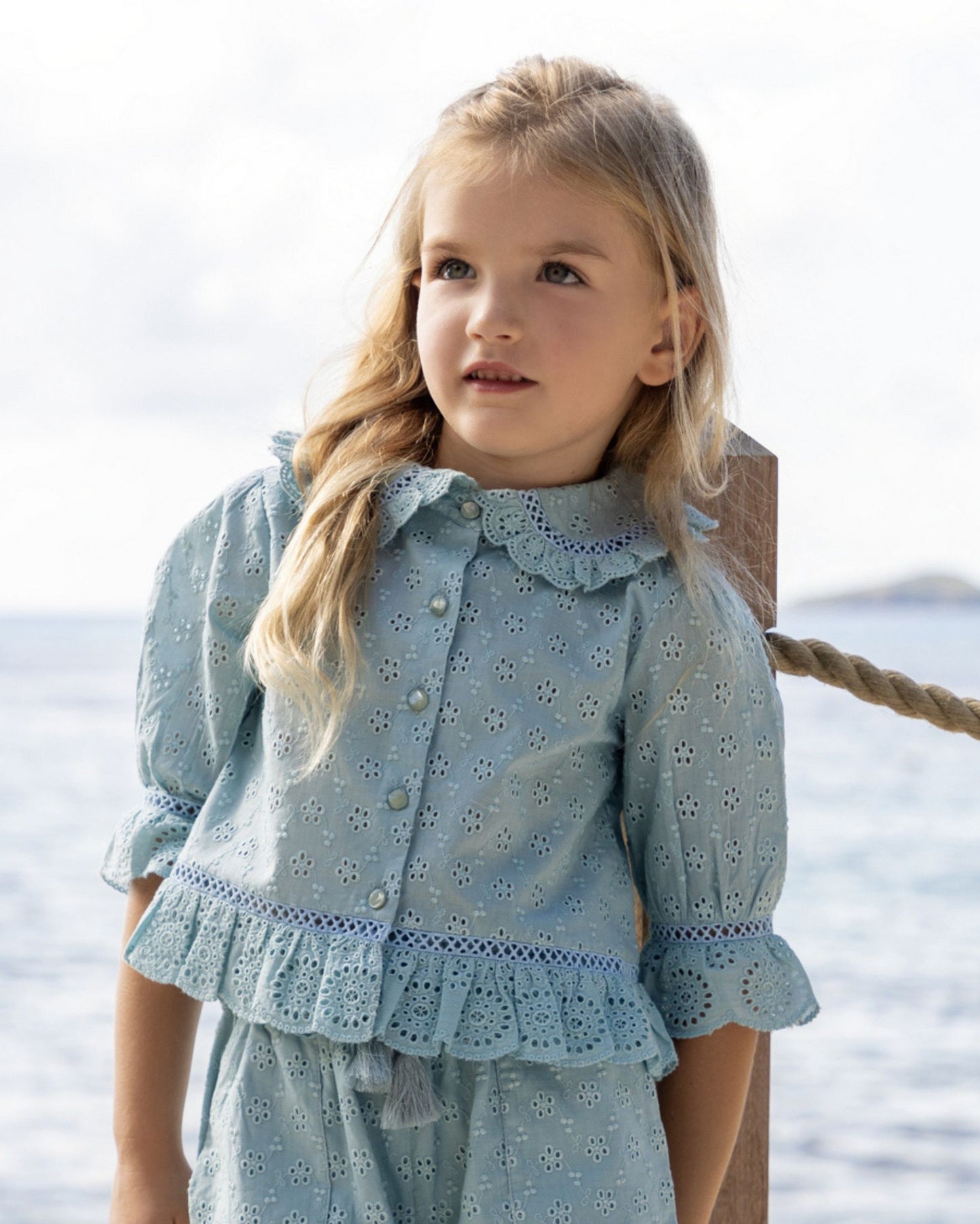 Early Sunday, Iris Blouse in Sea Dream color, made from All-Over Eyelet Embroidered Cotton Schifflie fabric, featuring relaxed fit with delicate detailing for a timeless and feminine look, shown in a close up view of model wearing outdoors