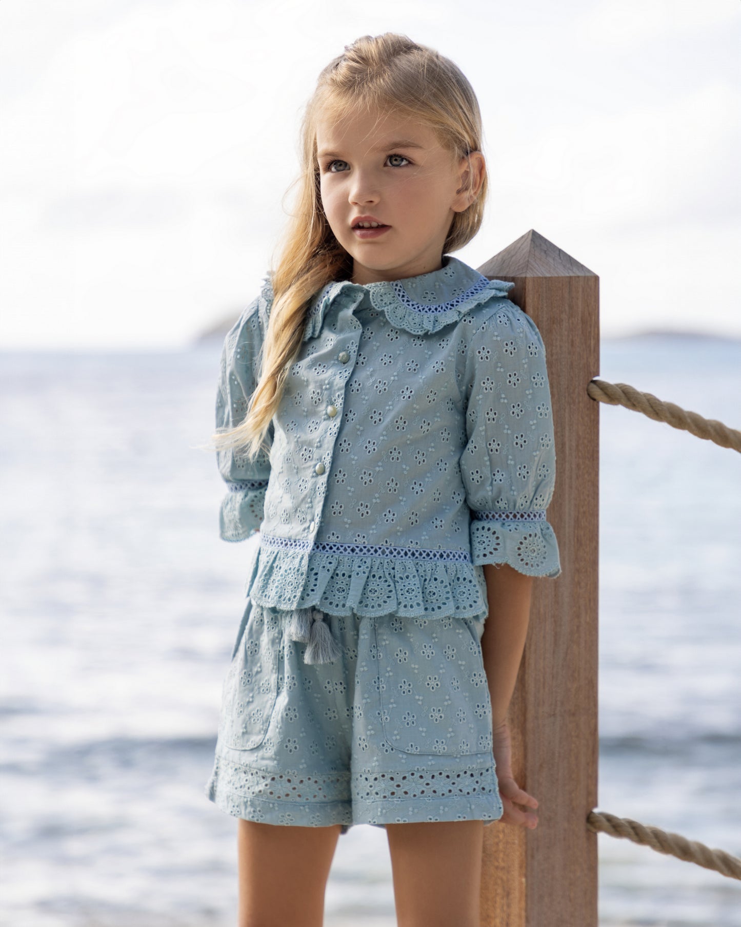 Early Sunday, Iris Blouse in Sea Dream color, made from All-Over Eyelet Embroidered Cotton Schifflie fabric, featuring relaxed fit with delicate detailing for a timeless and feminine look, shown in a front view of model wearing it