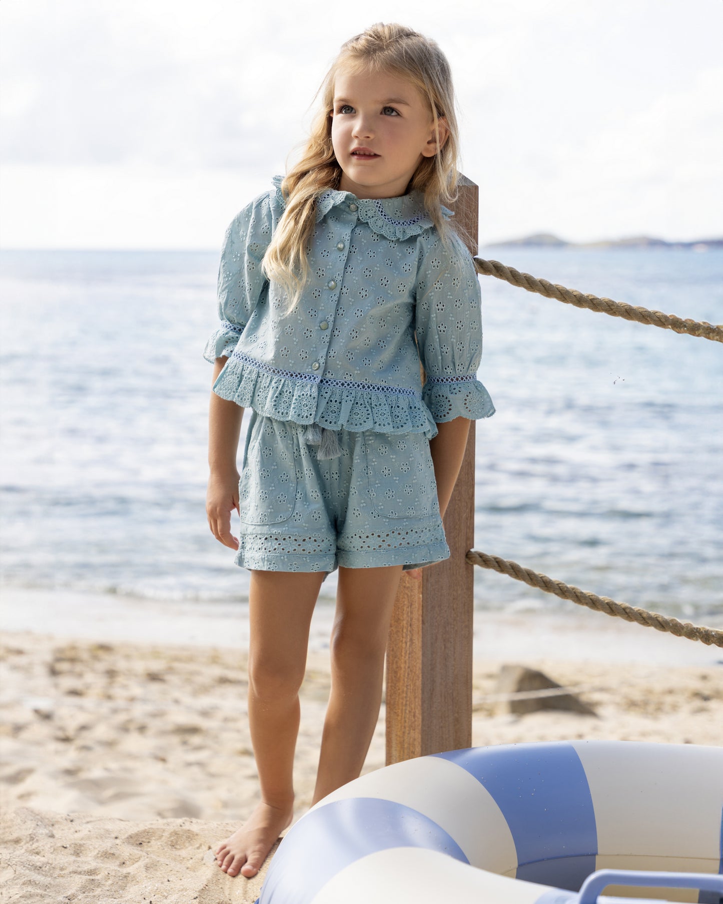 Early Sunday, Iris Blouse in Sea Dream color, made from All-Over Eyelet Embroidered Cotton Schifflie fabric, featuring relaxed fit with delicate detailing for a timeless and feminine look, shown in a front view of model wearing outdoors