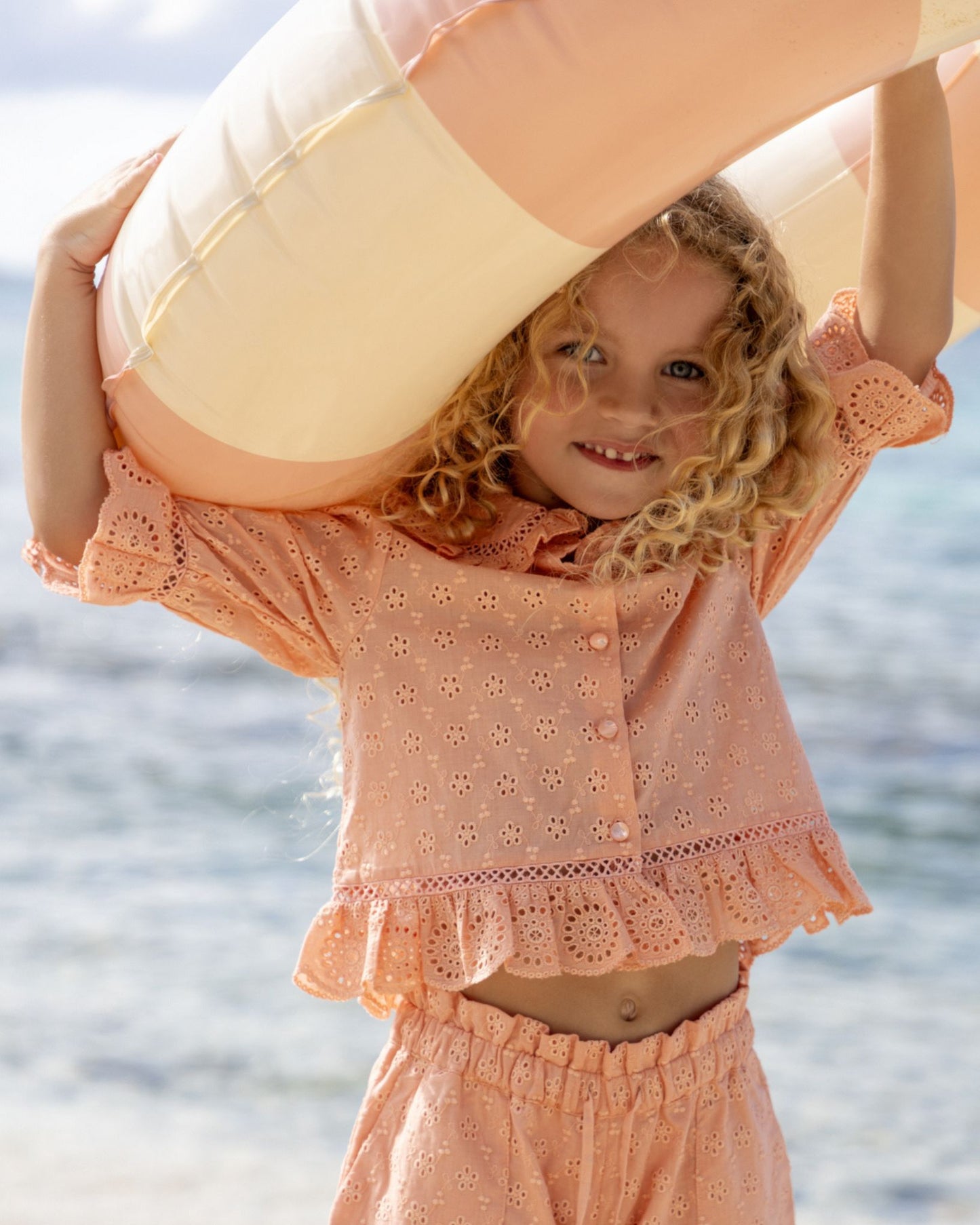 Early Sunday, Iris Blouse in Strawberry color, made from All-Over Eyelet Embroidered Cotton Schifflie fabric, featuring relaxed fit with delicate detailing for a timeless and feminine look, shown in a front view of model wearing outdoors