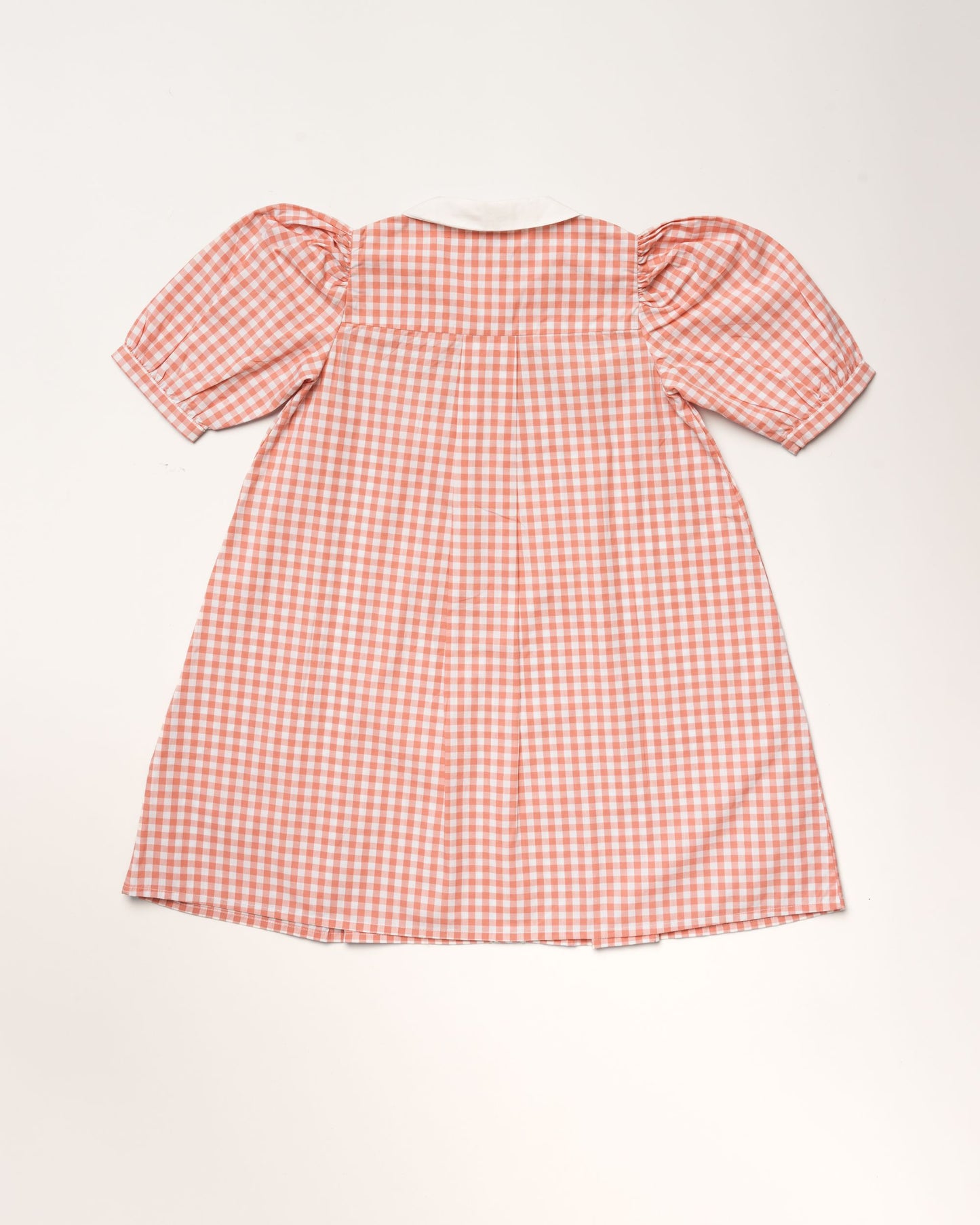 Early Sunday, Jane Dress in Peony color, made from 100% cotton gingham checks fabric, featuring Smocked / embroidered yoke, peter pan collar and puffed short sleeves, shown in a back flat-lay view