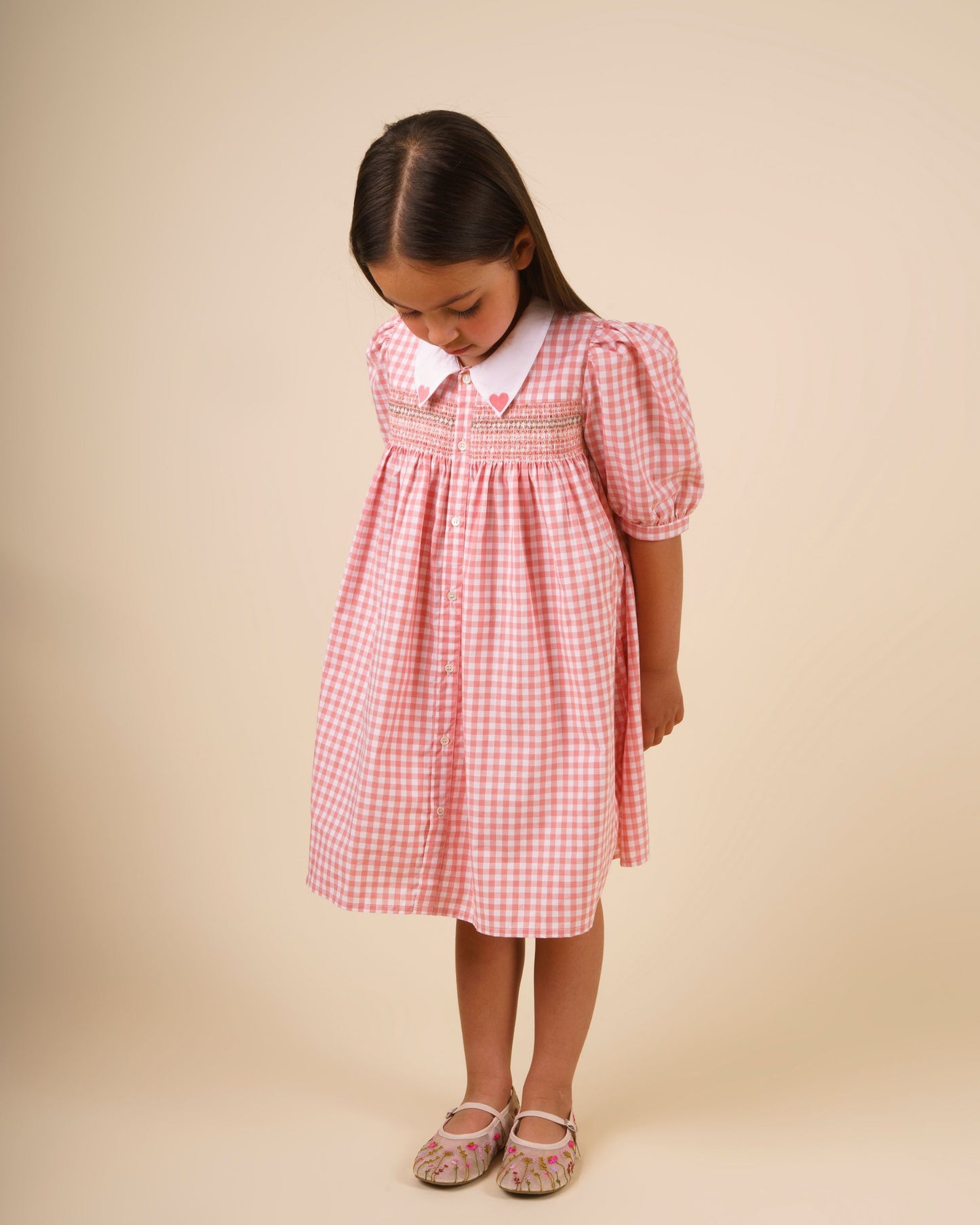 Early Sunday, Jane Dress in Peony color, made from 100% cotton gingham checks fabric, featuring Smocked / embroidered yoke, peter pan collar and puffed short sleeves, shown in a model standing facing front wearing