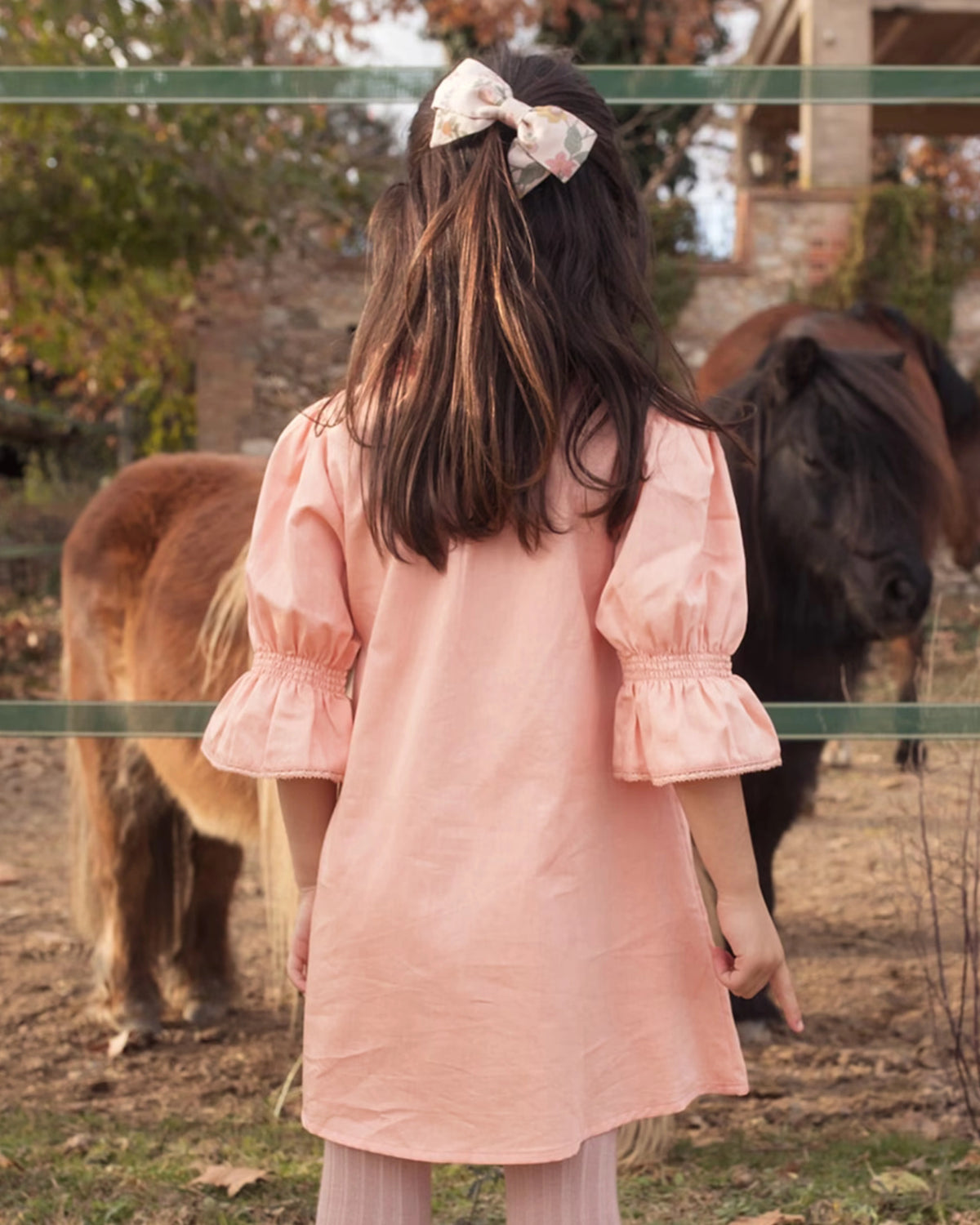 Early Sunday, Julie Dress in Blush Pink, made from Cotton Satin fabric, featuring cute floral embroidery on a Peter Pan collar with a smocked chest, shown in a back view of model wearing it
