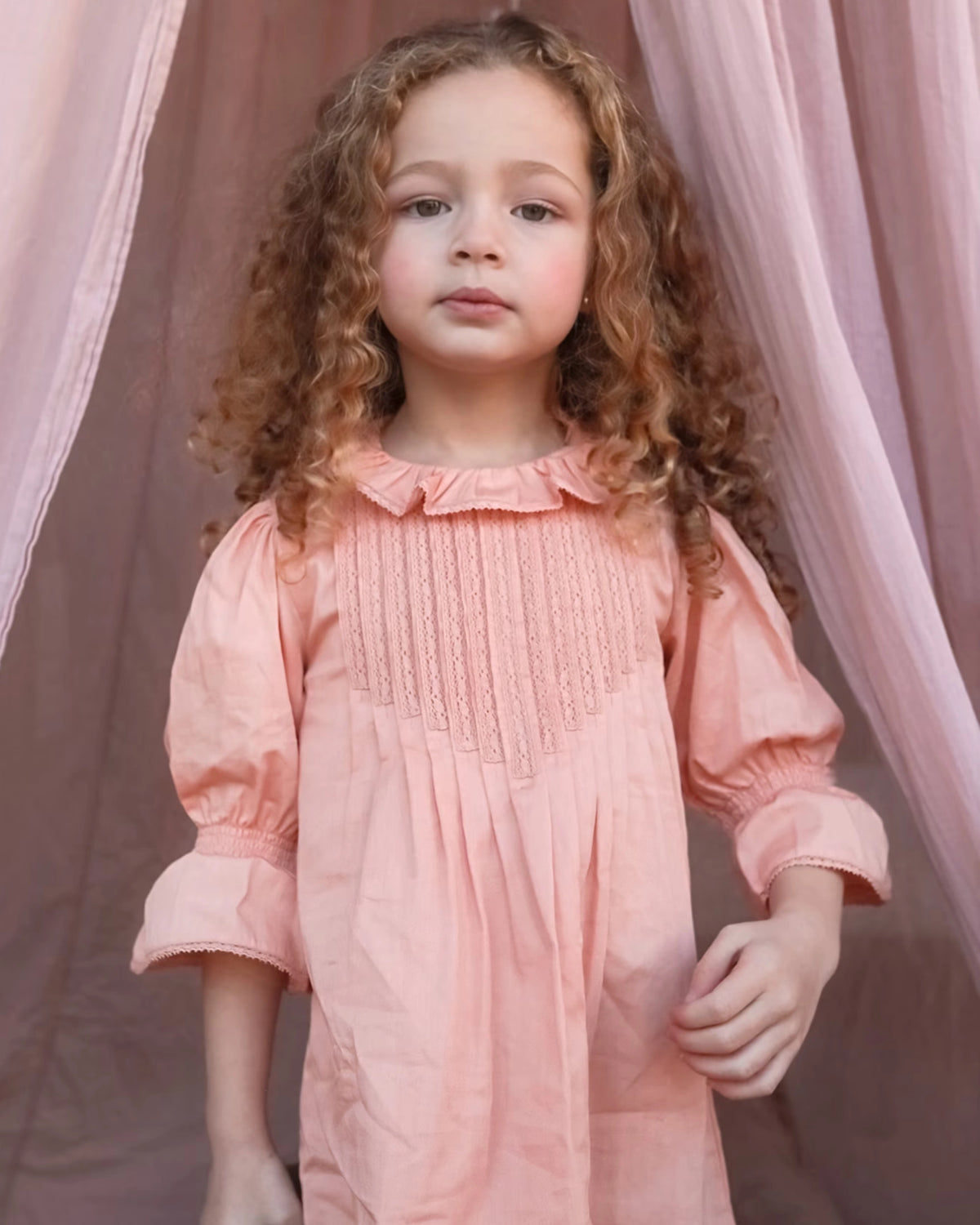 Early Sunday, Julie Dress in Blush Pink, made from Cotton Satin fabric, featuring cute floral embroidery on a Peter Pan collar with a smocked chest, shown in a close up shot of model wearing it