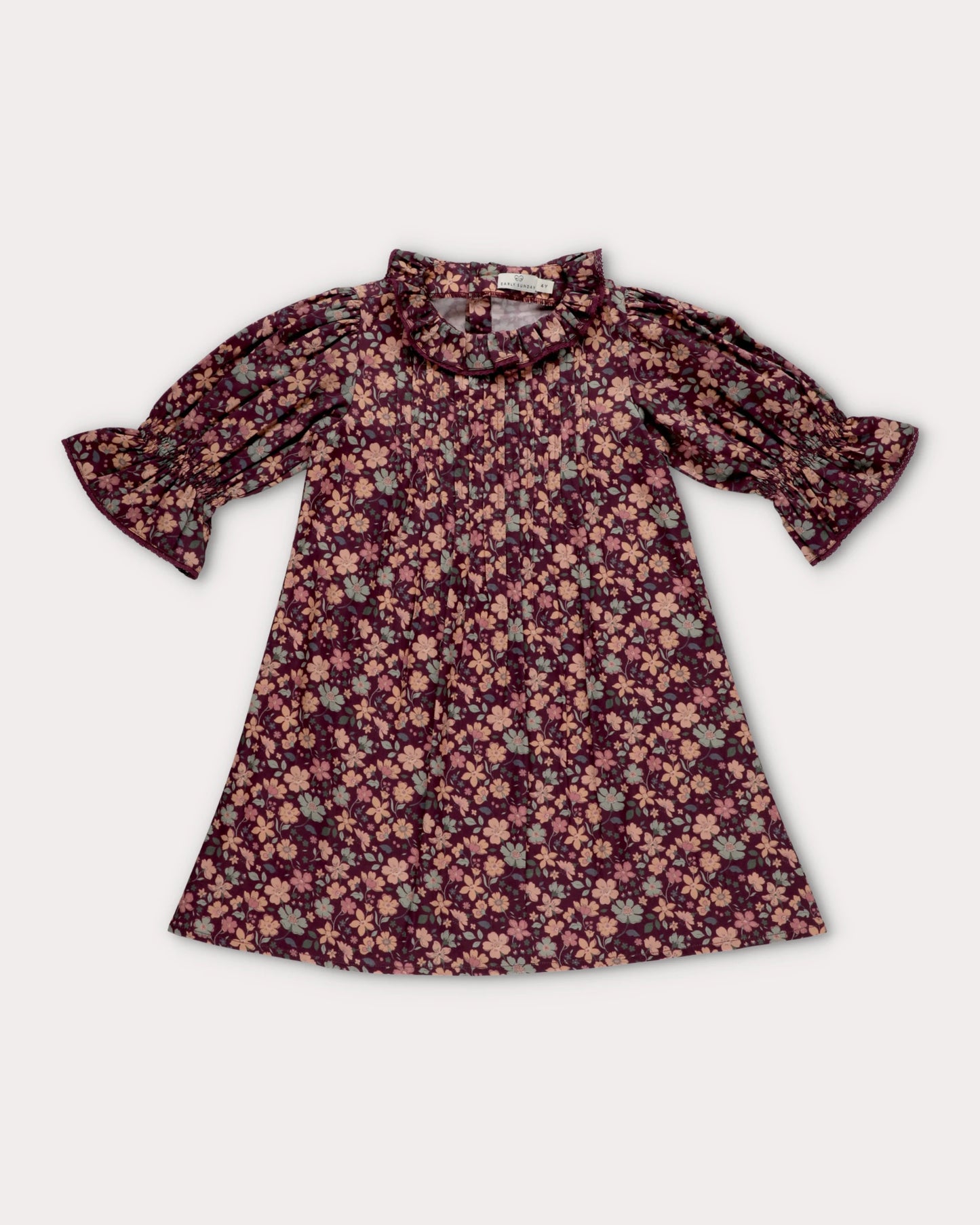 Early Sunday, Julie Dress in Plum, made from Printed Cotton Satin fabric, featuring detailed lace gathered sleeves with frilled neckline & floral detailing, shown in a front flat-lay view