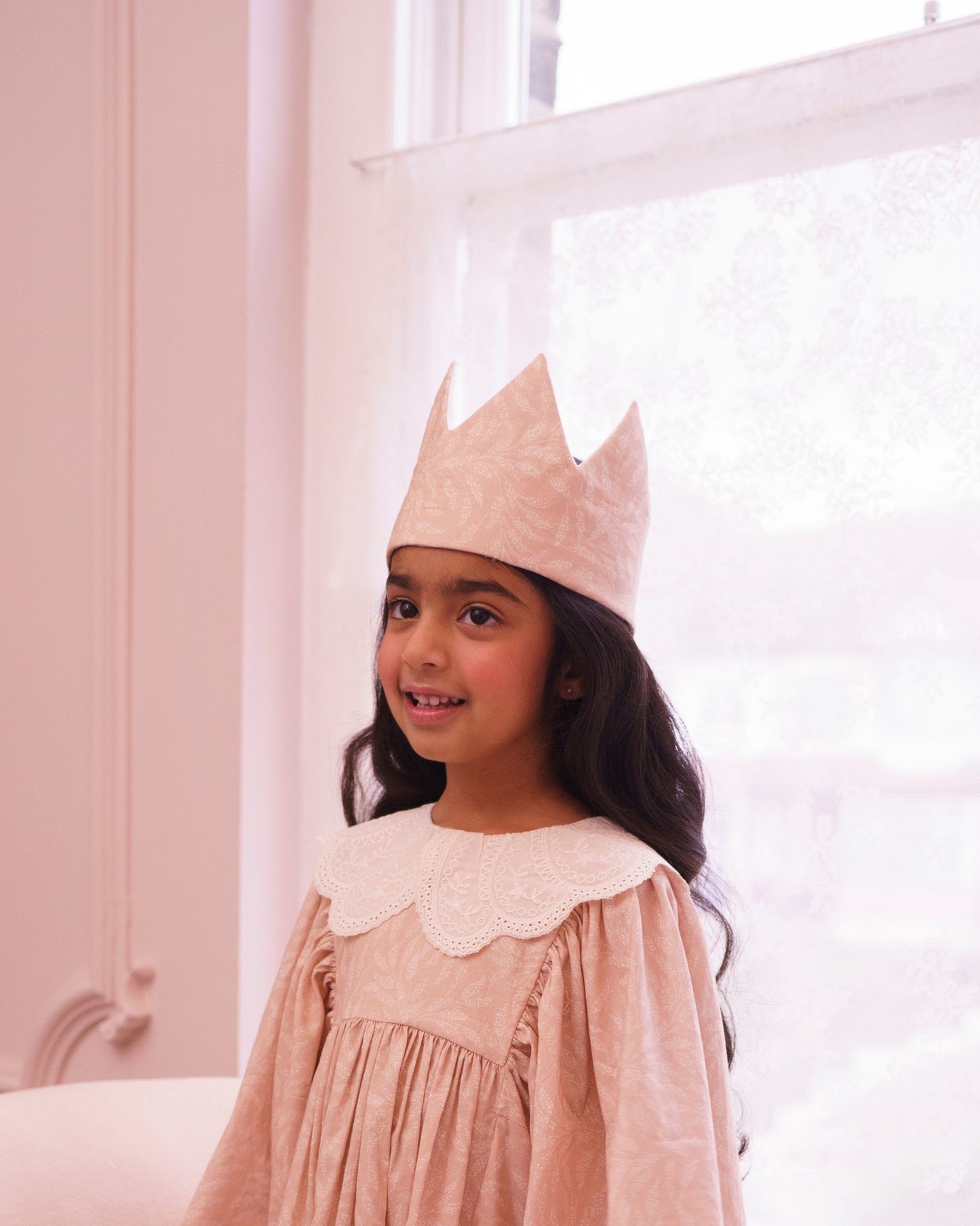 Early Sunday, Kids Crown in Feather print, made from Printed 60s Cotton Cambric fabric, featuring a design with pointed tips & an elasticated band, shown in an angled view of model wearing it in a close-up shot