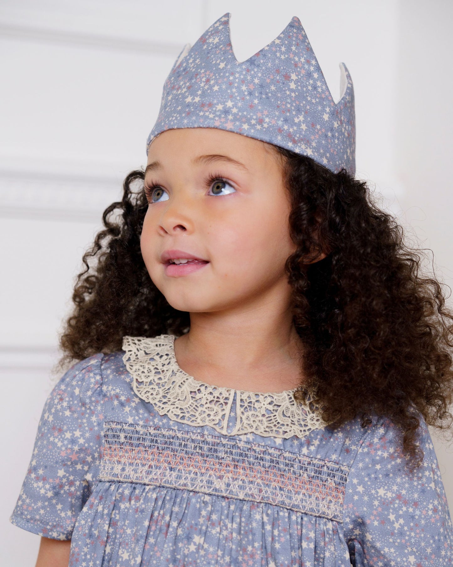 Early Sunday, Kids Crown in Celestial print, made from Printed 60s Cotton Satin fabric, featuring a design with pointed tips & an elasticated band, shown in a close up shot of model wearing it