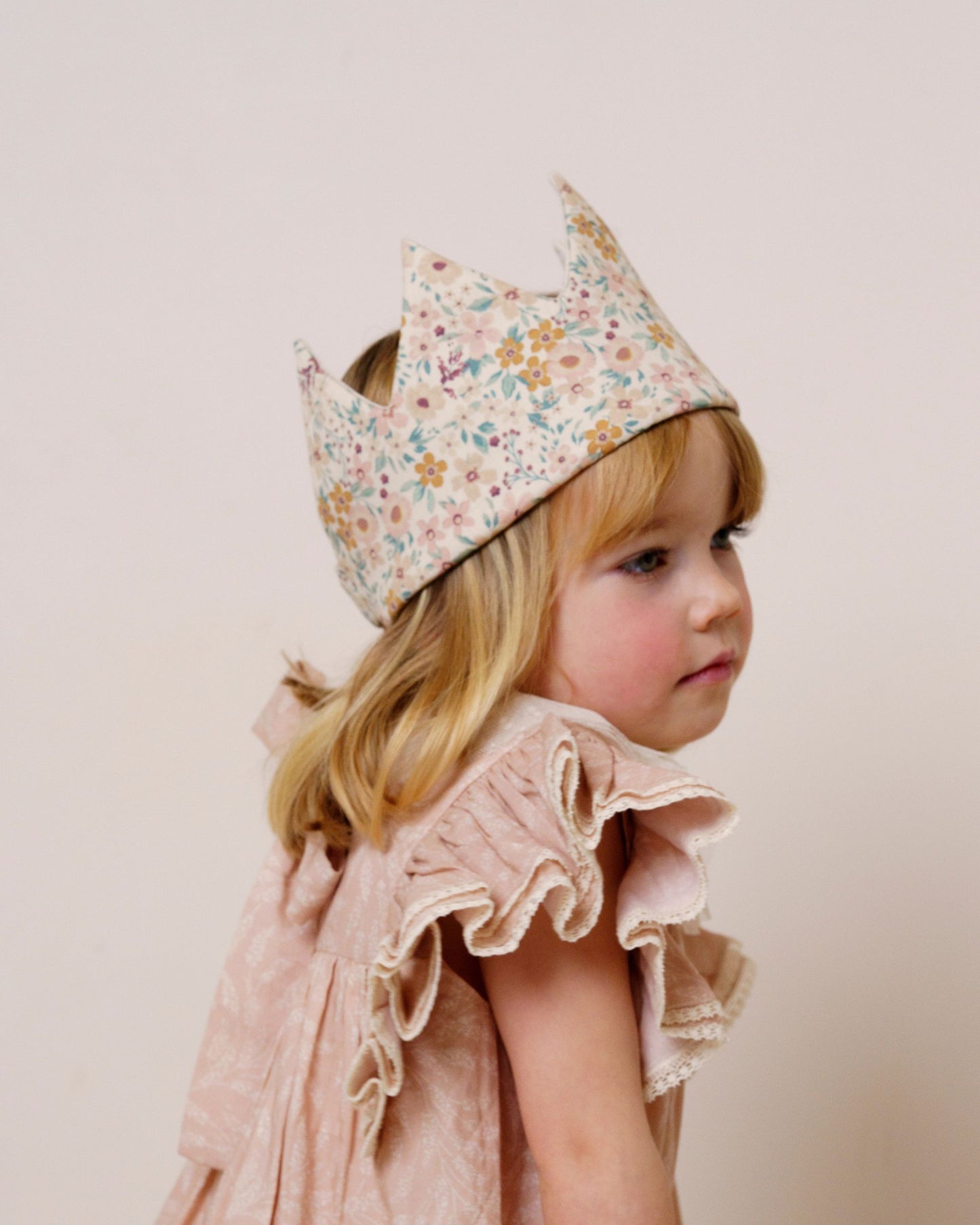 Early Sunday, Kids Crown in Floral print, made from Printed 60s Cotton Satin fabric, featuring a design with pointed tips & an elasticated band, shown in a close-up side view of a model wearing it
