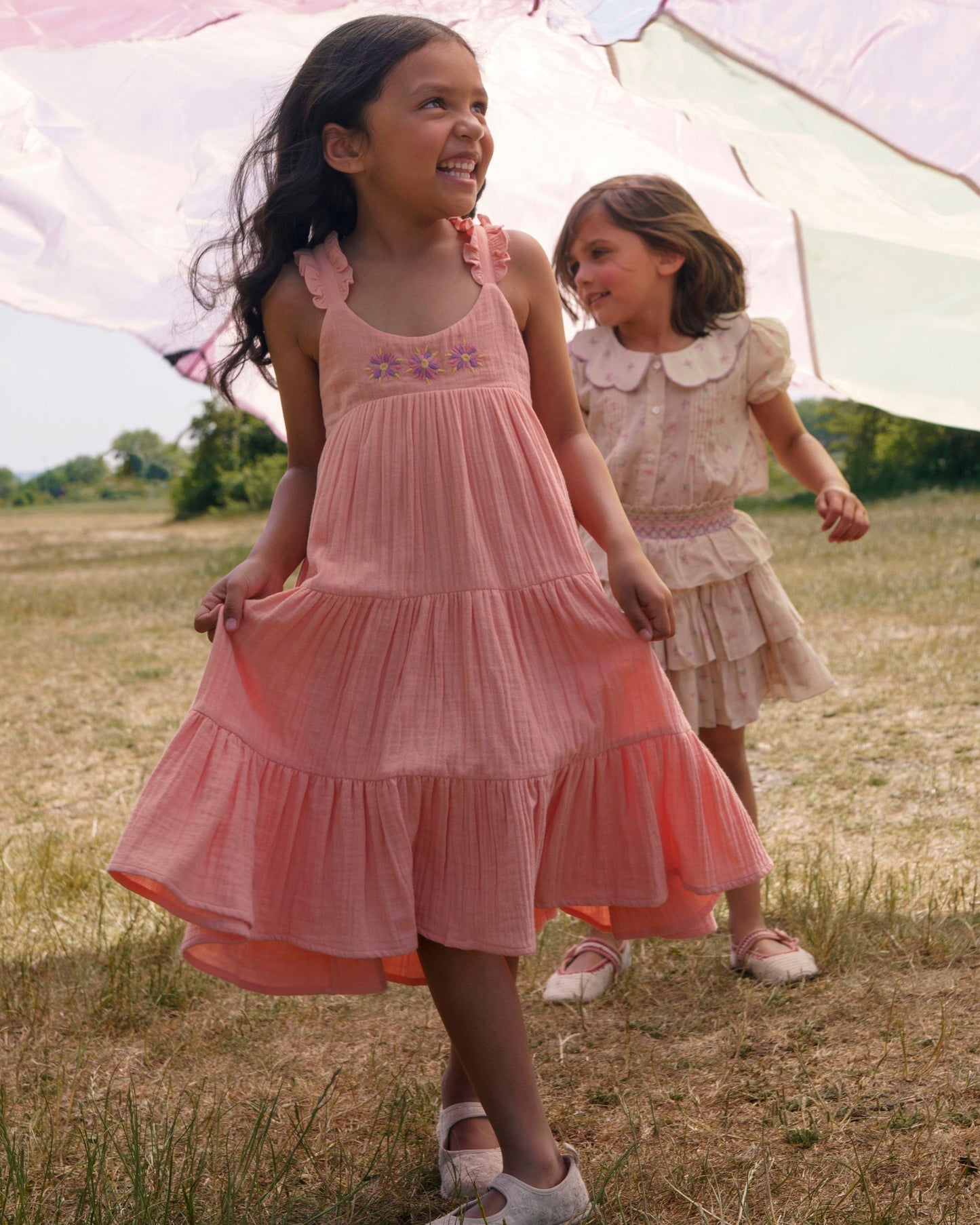Early Sunday, Laura Dress in Candy Floss color, made from 100% cotton double gauze solid fabric, featuring Crisscross ruffle straps with delicate trim accents and a softly gathered tiered skirt, shown in a Model walking / movement shot