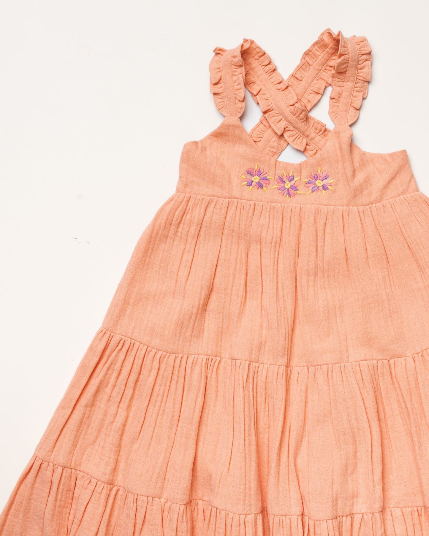 Early Sunday, Laura Dress in Candy Floss color, made from 100% cotton double gauze solid fabric, featuring Crisscross ruffle straps with delicate trim accents and a softly gathered tiered skirt, shown in a closeup flat-lay view