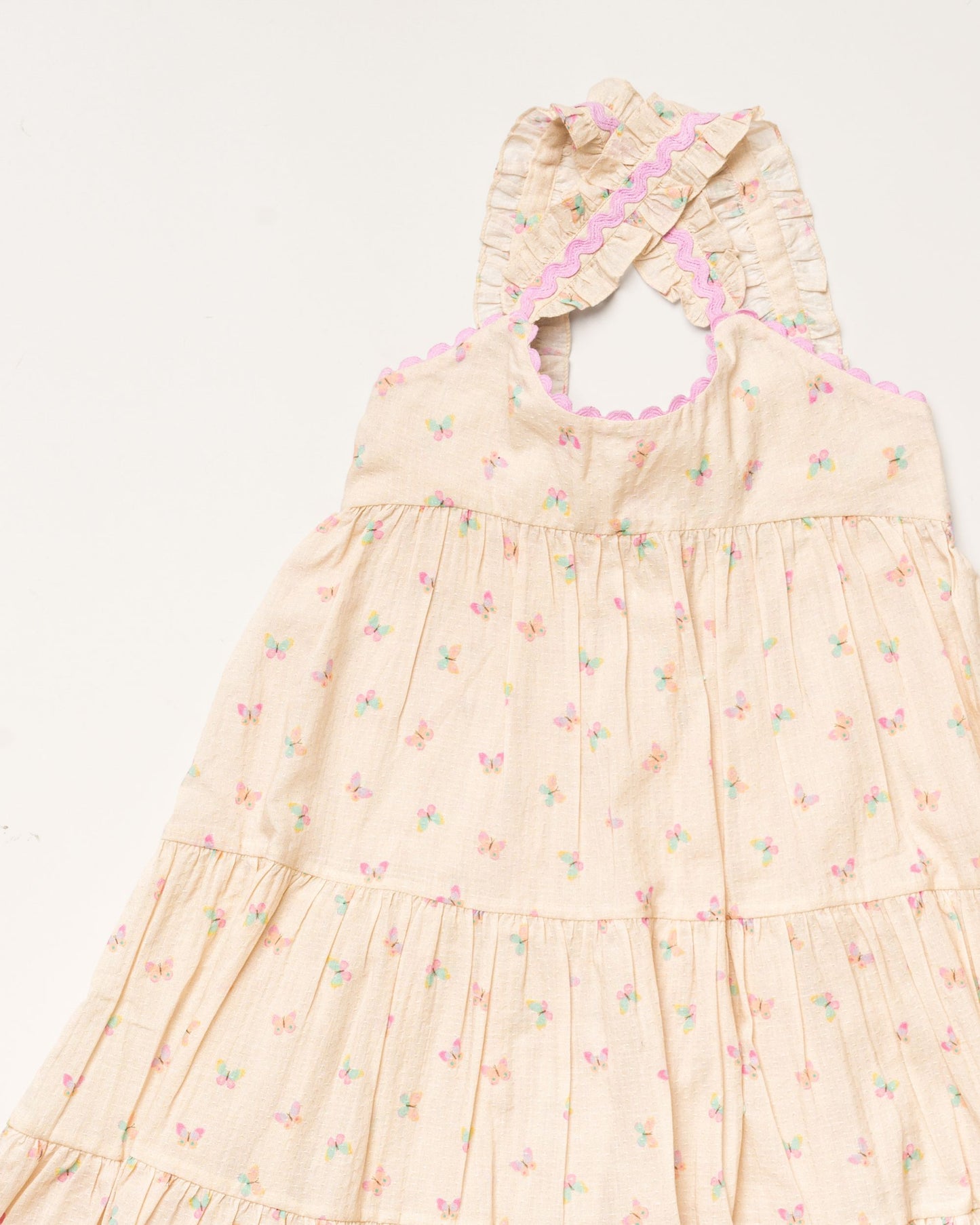 Early Sunday, Laura Dress in Butterfly Print color, made from printed cotton tiny swiss dobby fabric, featuring Crisscross ruffle straps with delicate trim accents and a softly gathered tiered skirt, shown in a closeup flat-lay view
