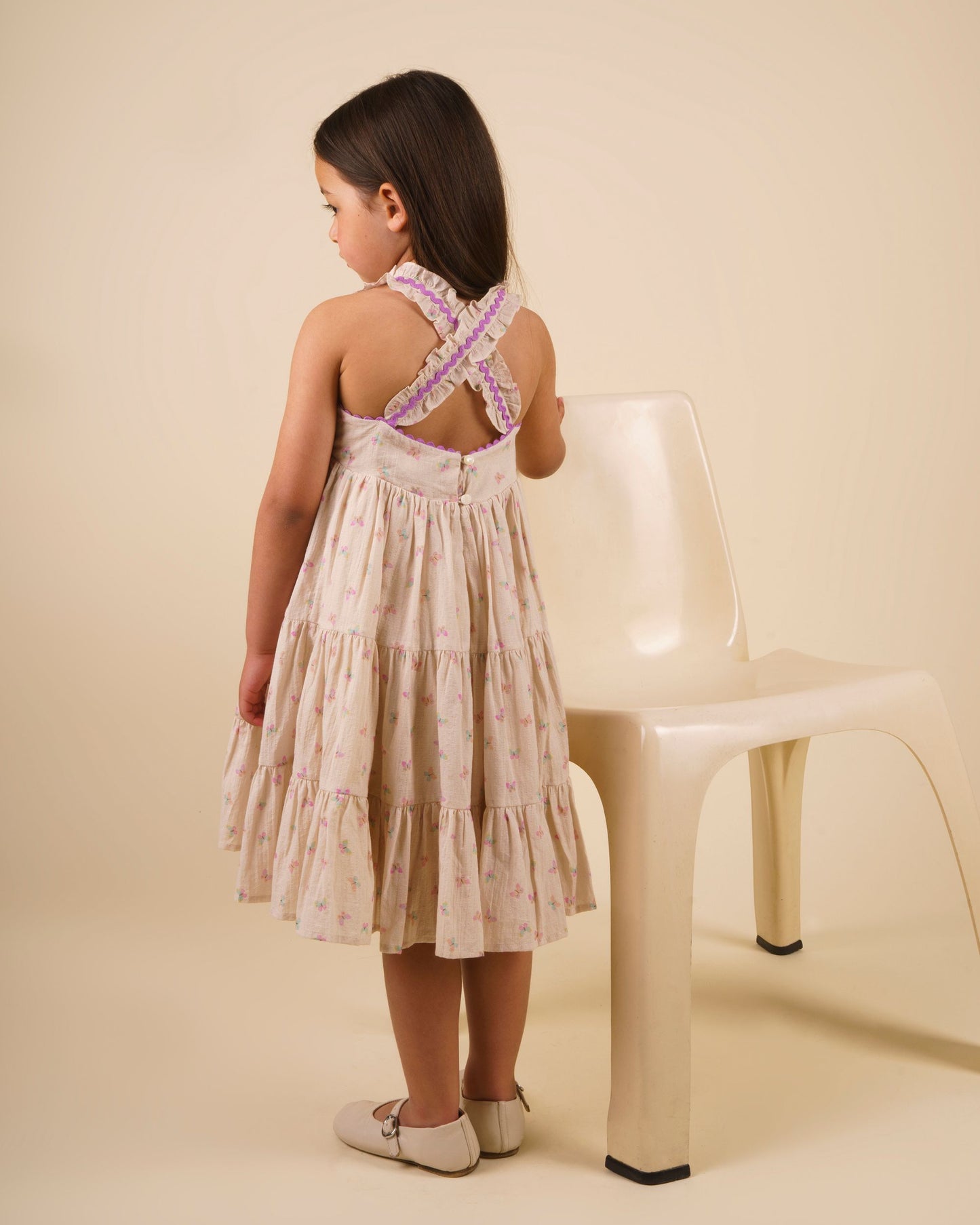 Early Sunday, Laura Dress in Butterfly Print color, made from printed cotton tiny swiss dobby fabric, featuring Crisscross ruffle straps with delicate trim accents and a softly gathered tiered skirt, shown in a back view of model wearing it